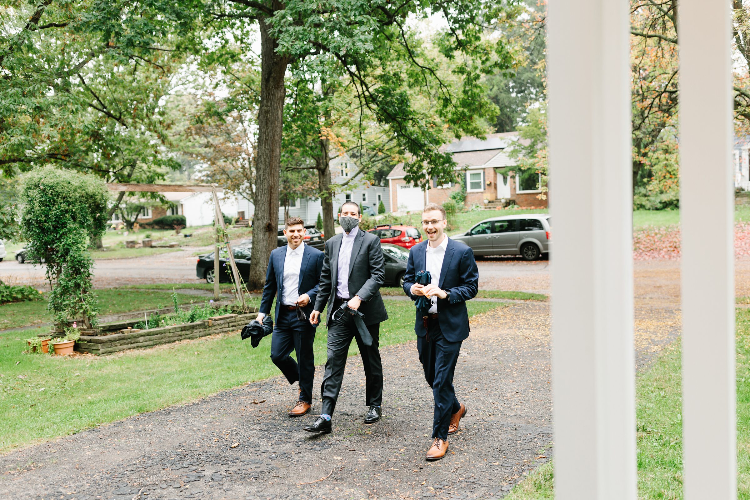 Groomsmen walk together outside holding their neckties by Detroit Wedding Photographer Michele Maloney