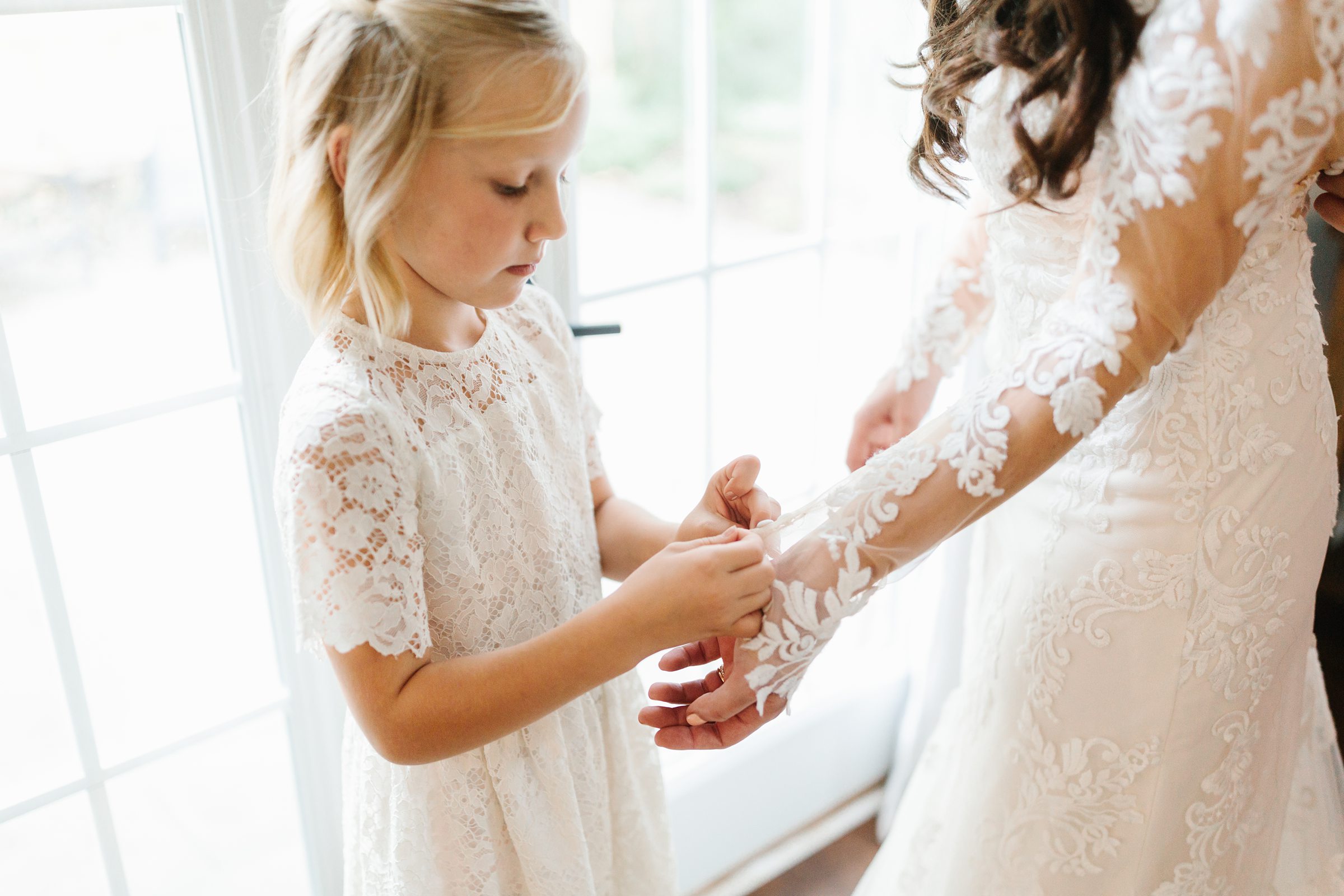 Close up of flower girl helping to button bride's sleeve by Detroit Wedding Photographer Michele Maloney 