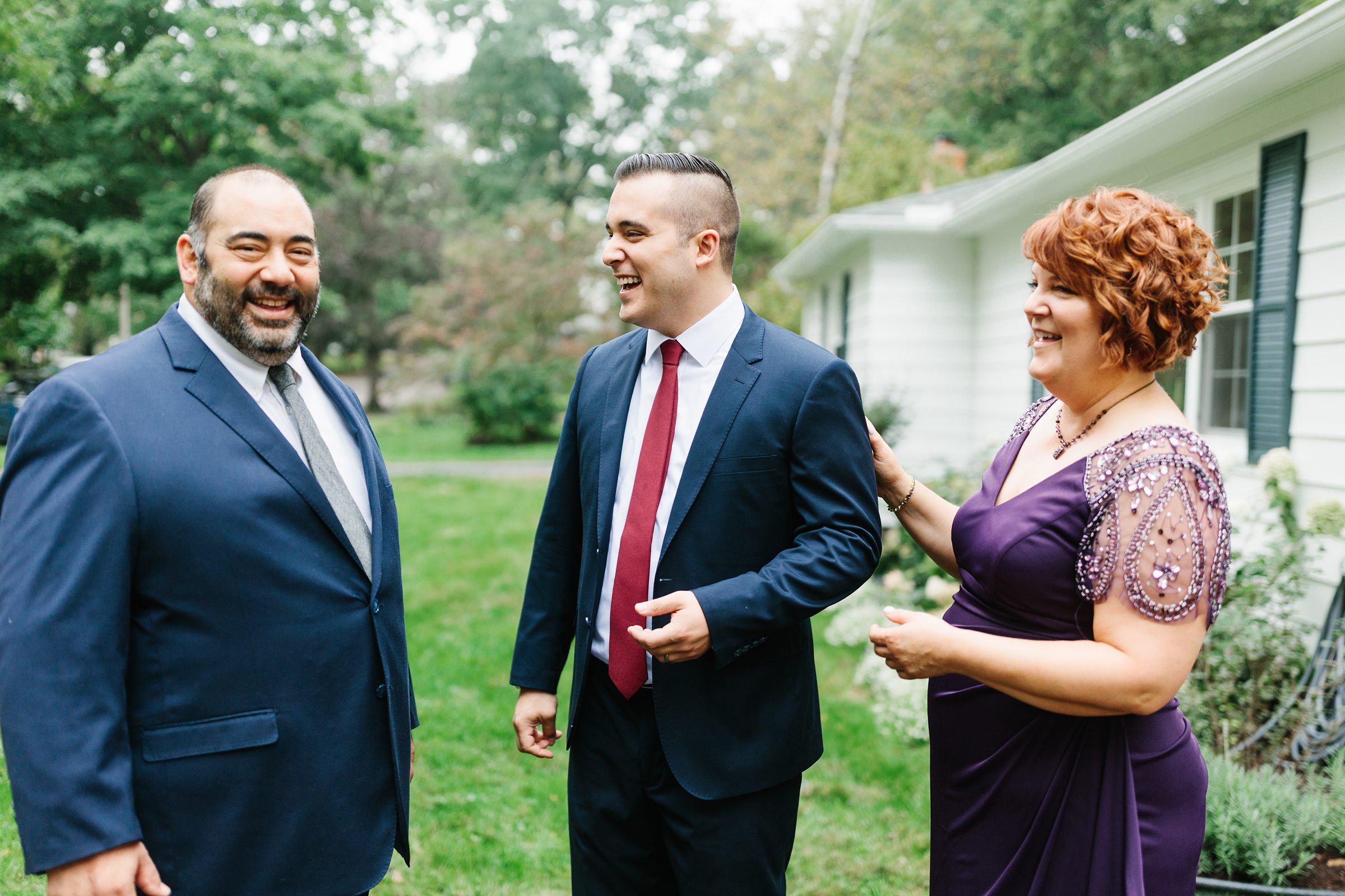 Groom is laughing surrounded by loved ones outside a house for the Ann Arbor intimate wedding by Detroit Wedding Photographer Michele Maloney
