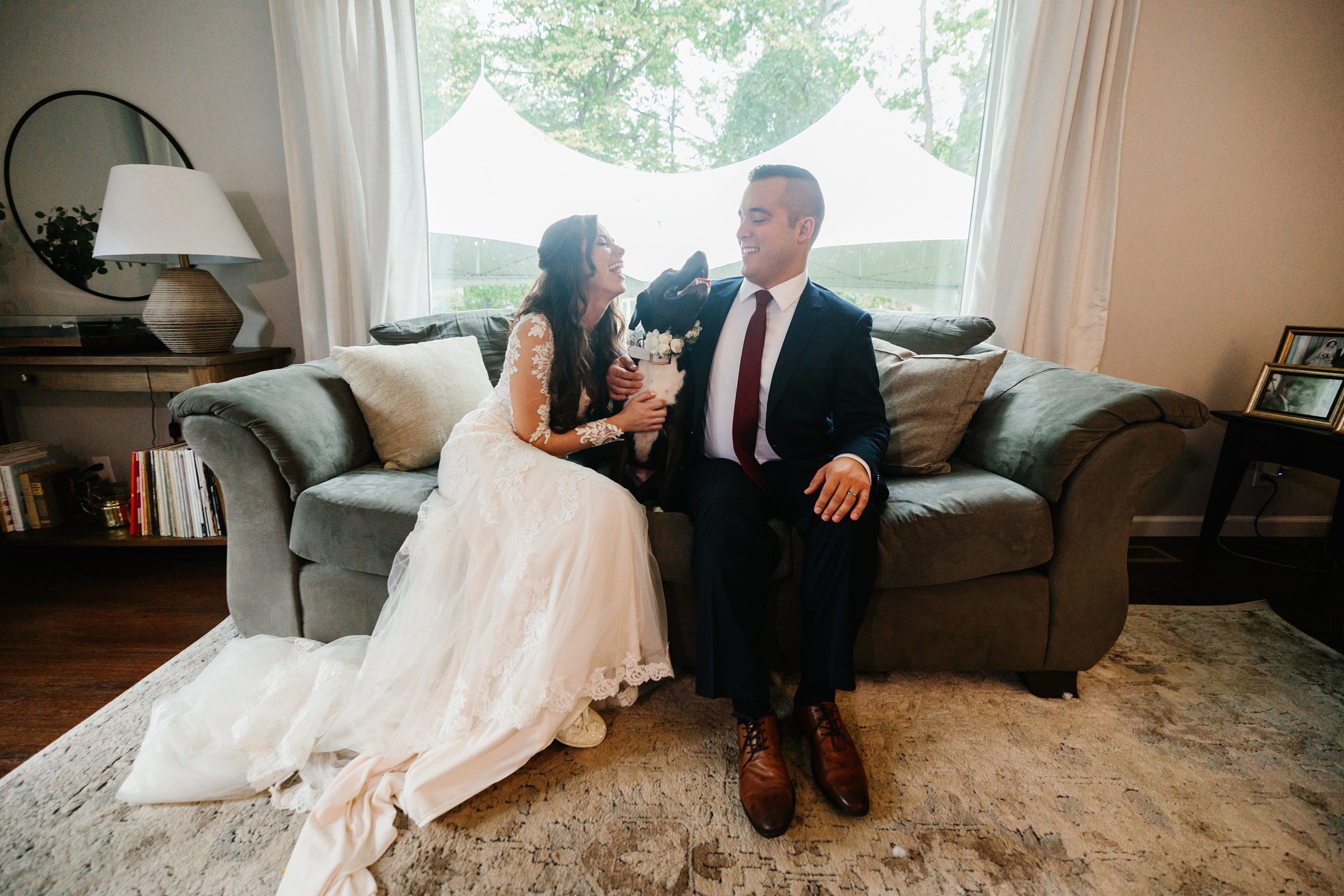 Bride and groom sit together on a couch in their home while petting their dog by Detroit Wedding Photographer Michele Maloney 