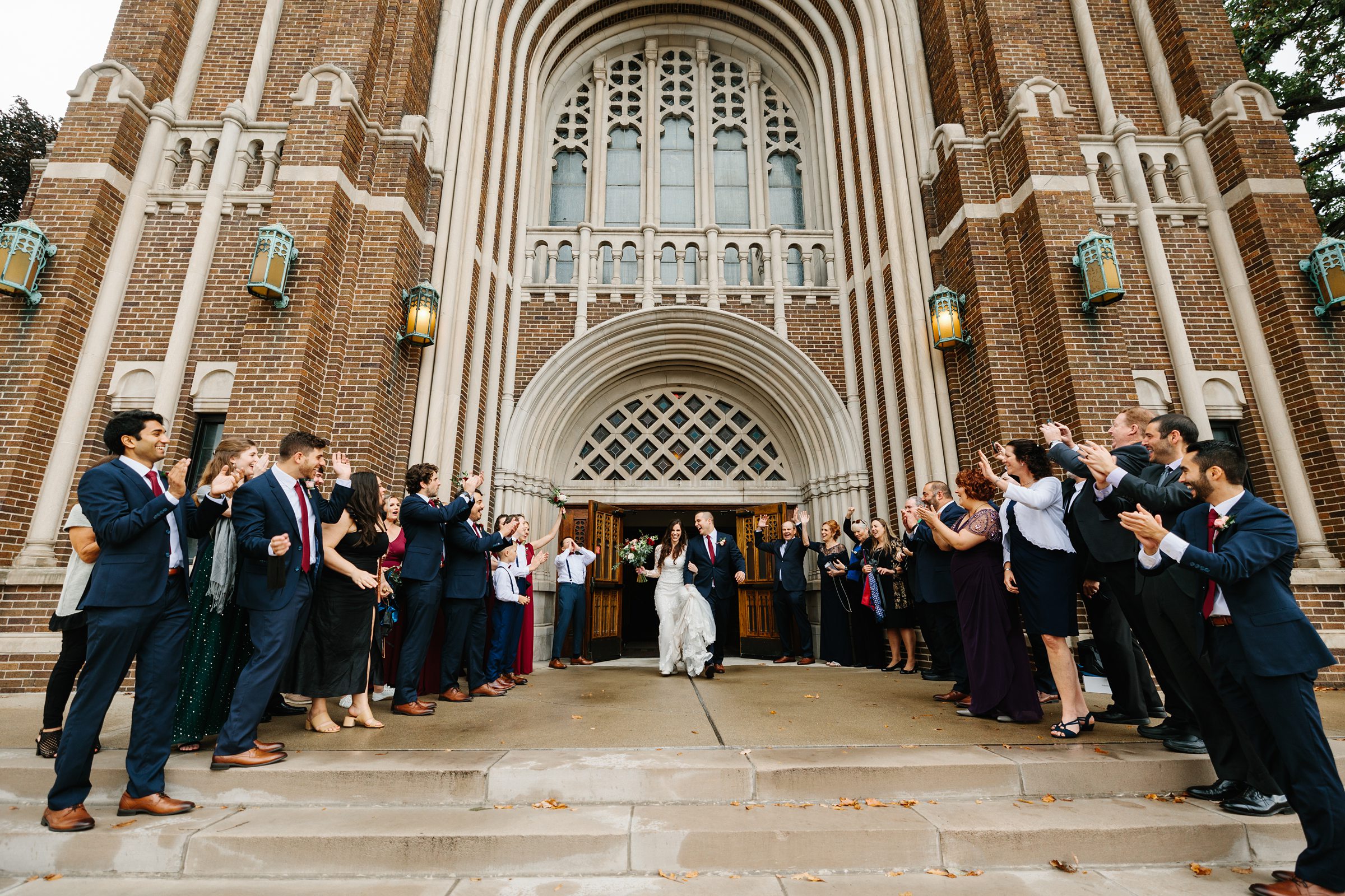 Faraway shot of the bridal party and guests lined up outside the church as they clap and cheer for the bride and groom exiting their ceremony for the Ann Arbor intimate wedding by Detroit Wedding Photographer Michele Maloney