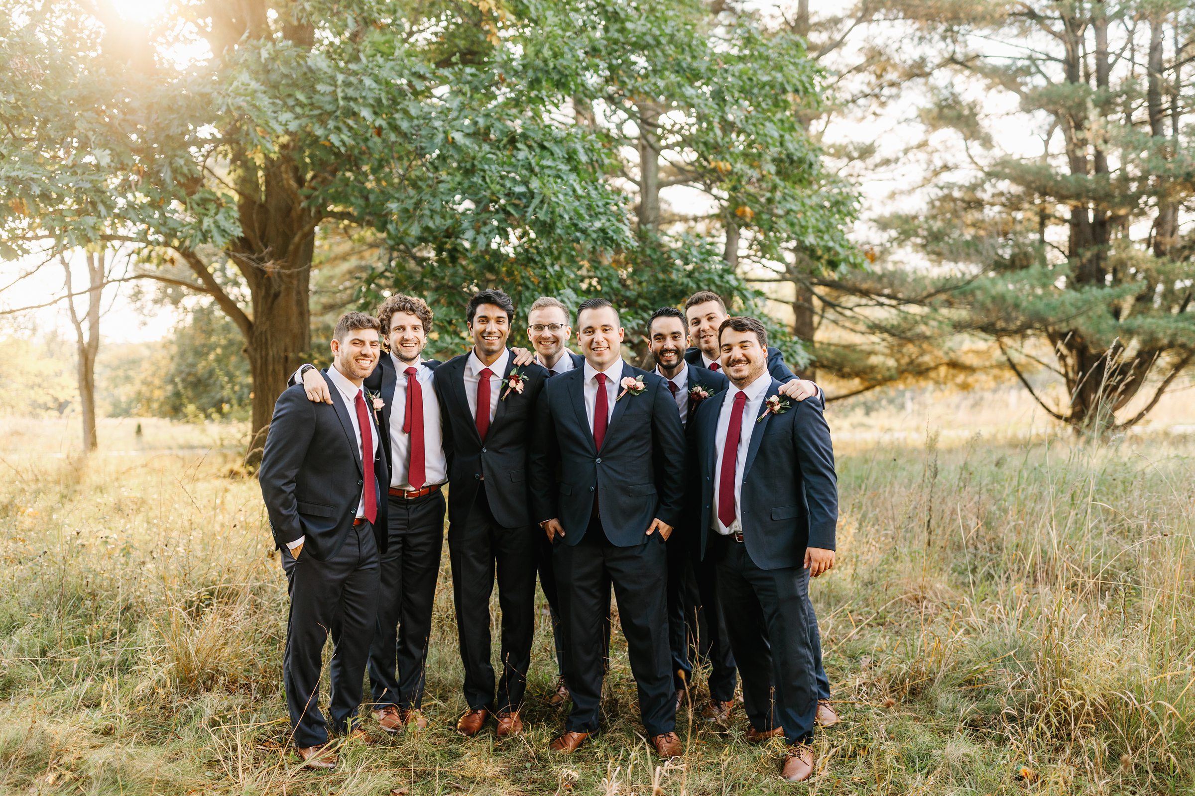 Groomsmen and groom smile together for portraits out in the woods by Detroit Wedding Photographer Michele Maloney