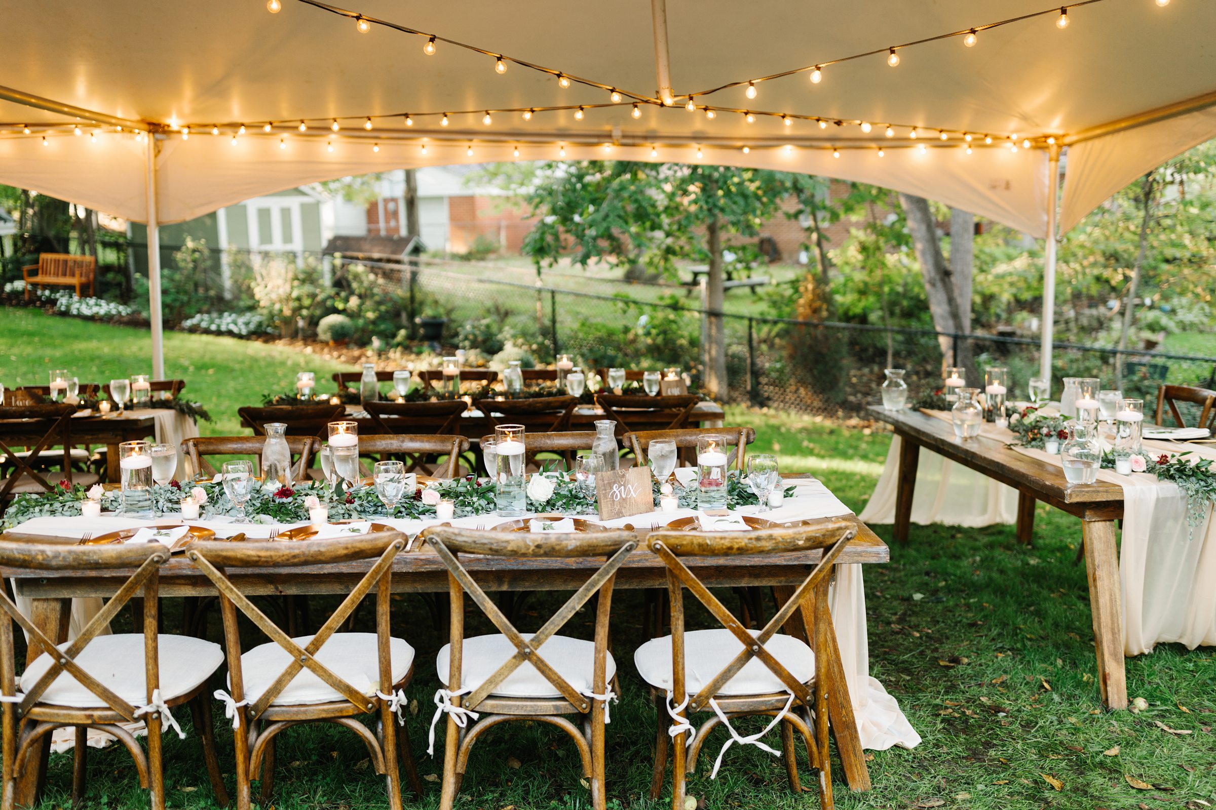 Detail photo of backyard wedding reception under a tent canopy with cafe lights, table settings are displayed by Detroit Wedding Photographer Michele Maloney
