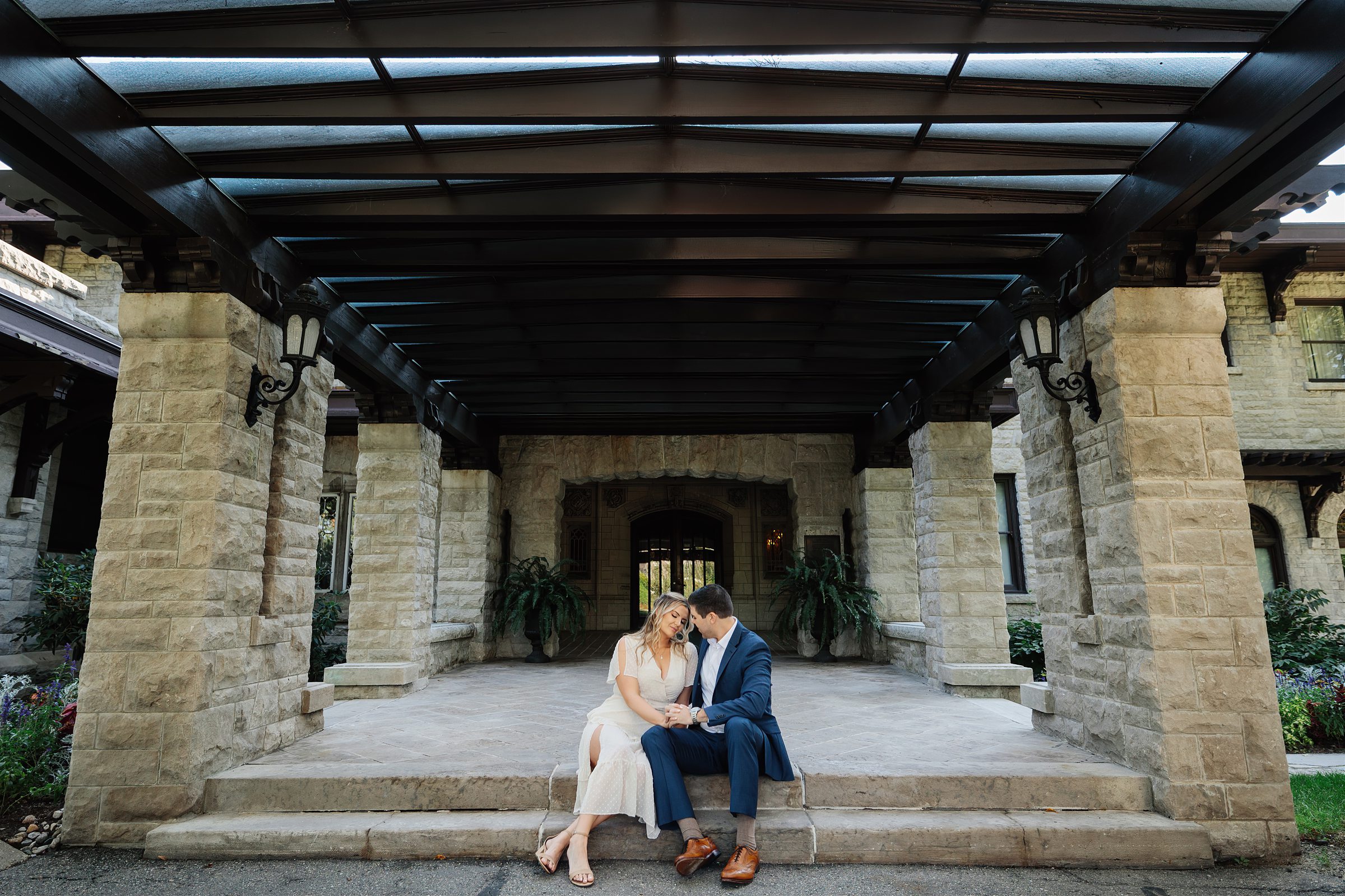 Engaged couple sits on steps outside for their Henry Ford Fair Lane engagement session by Detroit Wedding Photographer Michele Maloney