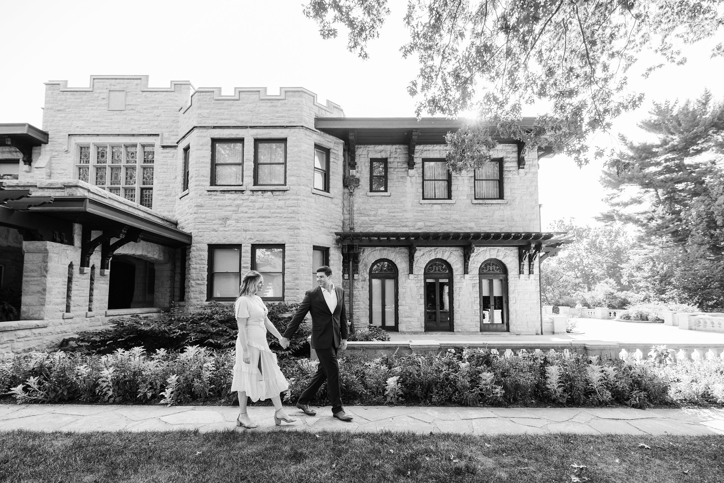 Black and white photo of engaged couple holding hands and taking a stroll for their Henry Ford Fair Lane engagement session by Detroit Wedding Photographer Michele Maloney