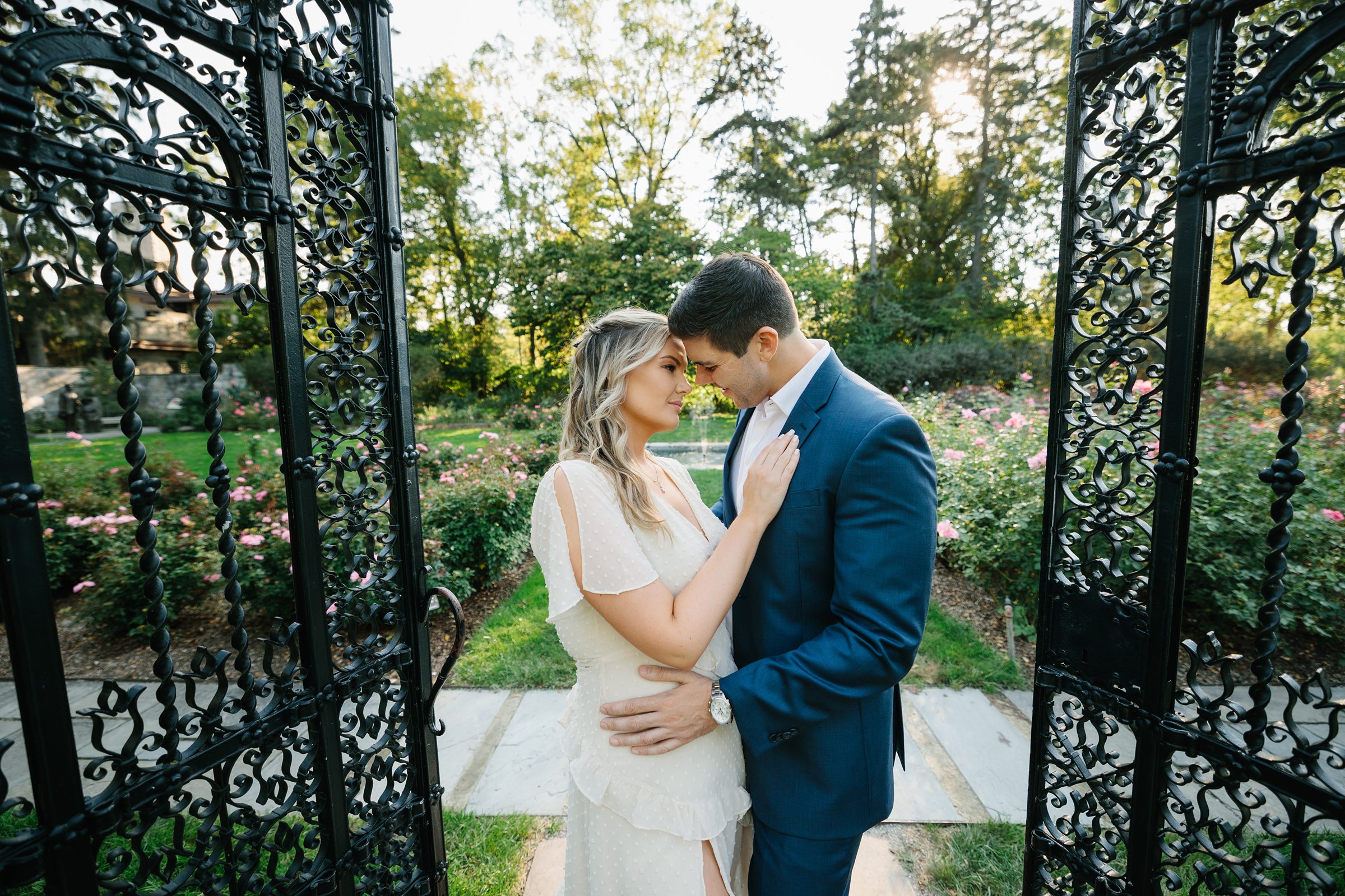 Engaged couple holds each other close and looks at each other in the middle of an open gate outside by Detroit Wedding Photographer Michele Maloney