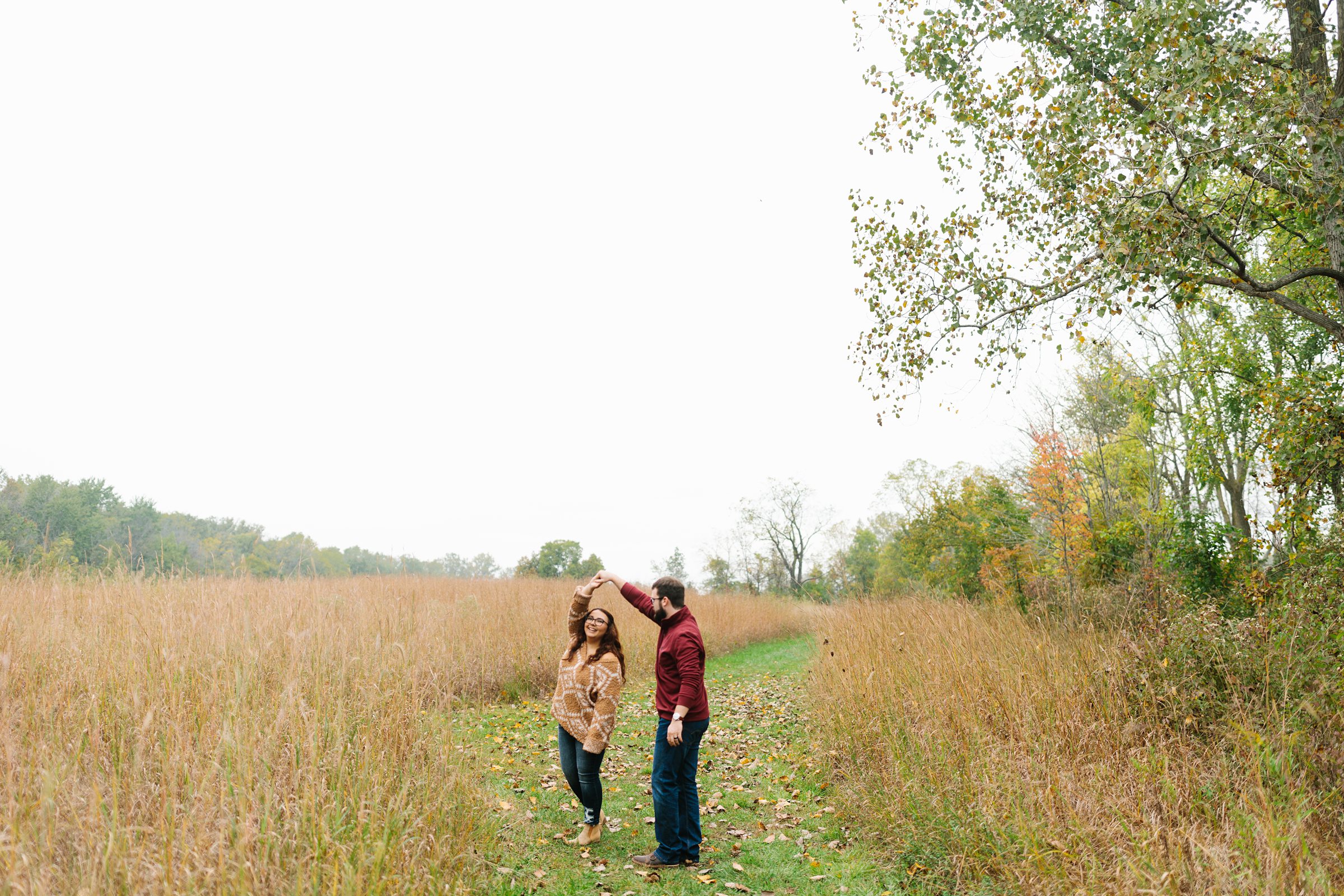 Engaged couple dances in grassy path for a fall engagement session by Detroit Wedding Photographer Michele Maloney