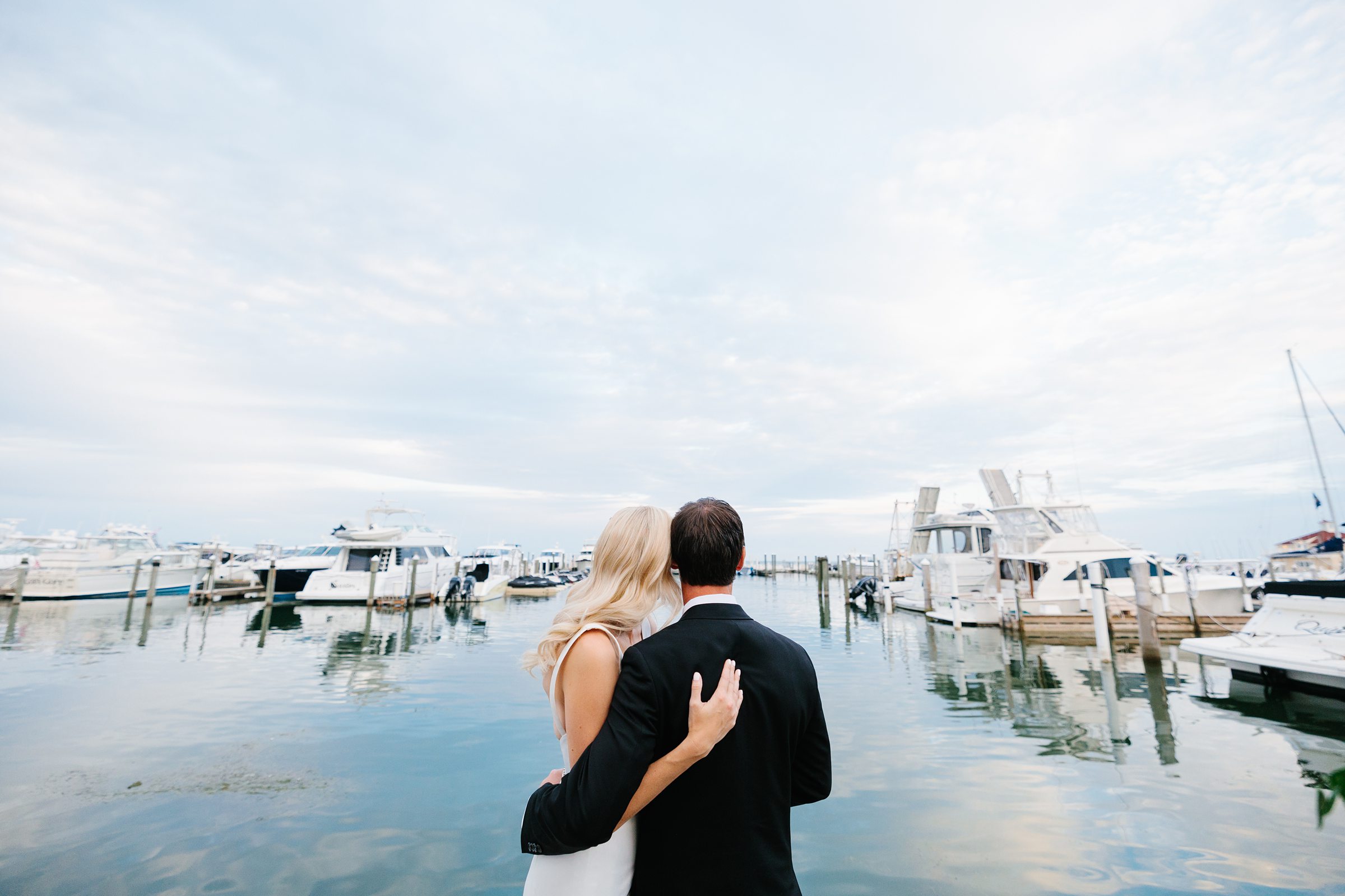 Shot from behind bride and groom, hugging as they look out at the water at the Grosse Pointe Yacht Club by Detroit Wedding Photographer Michele Maloney 