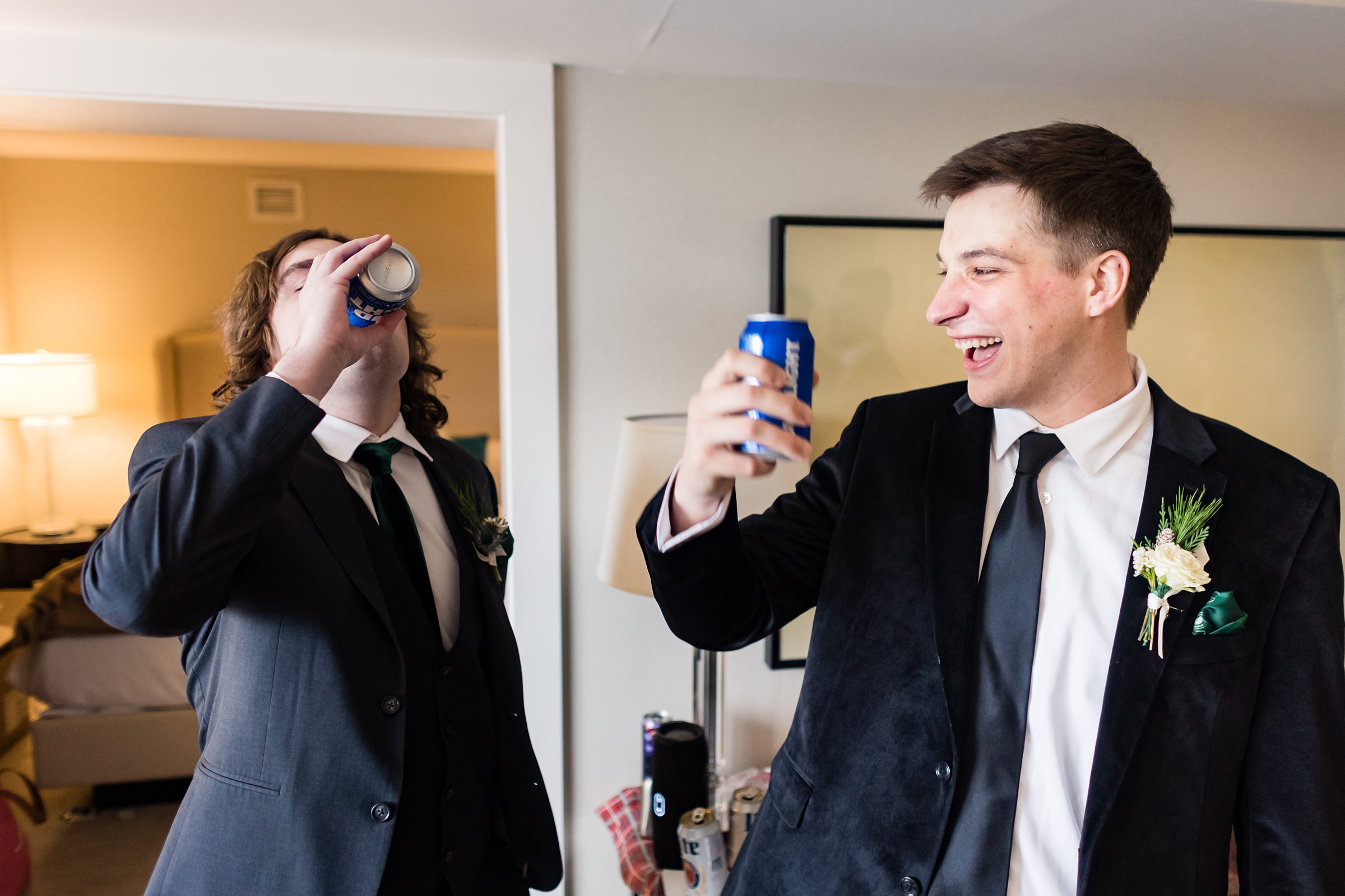 Groom and his groomsmen sip beer and laugh while getting ready by Detroit Wedding Photographer Michele Maloney