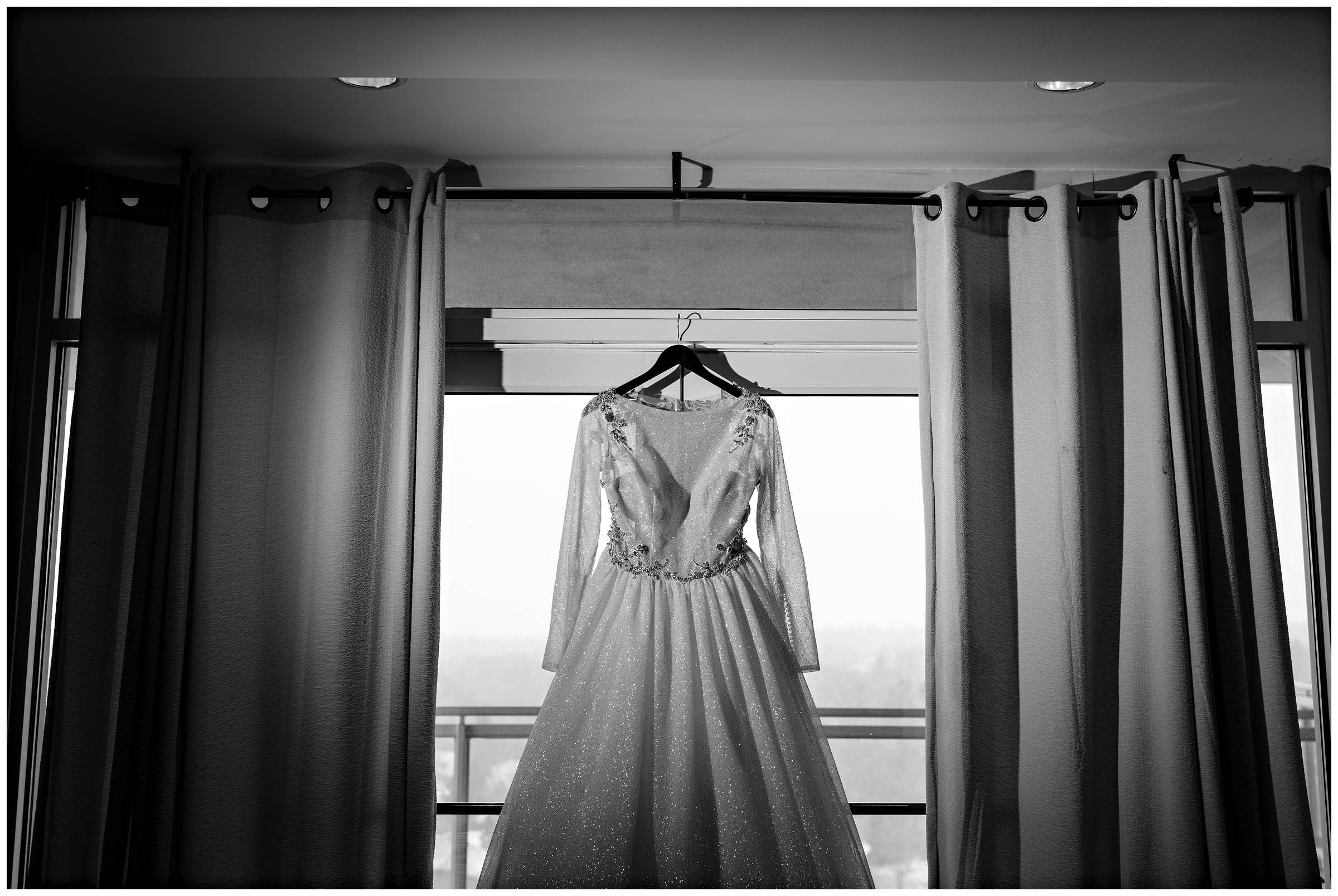 Faraway black and white picture of bride's wedding dress hanging from a window by Detroit Wedding Photographer Michele Maloney