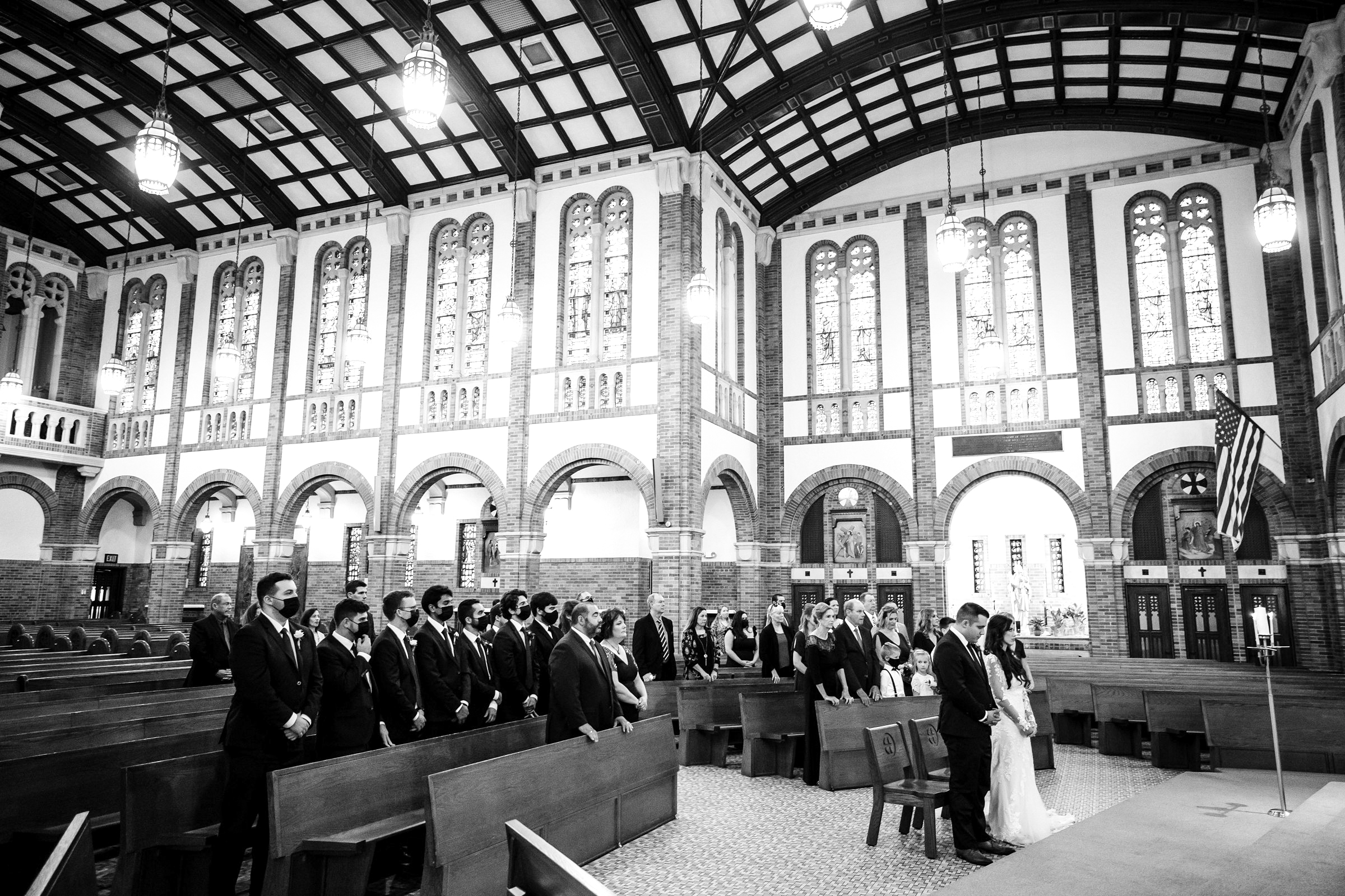 Faraway black and white photo of the bridal party and bride and groom facing the stage for the wedding ceremony by Detroit Wedding Photographer Michele Maloney