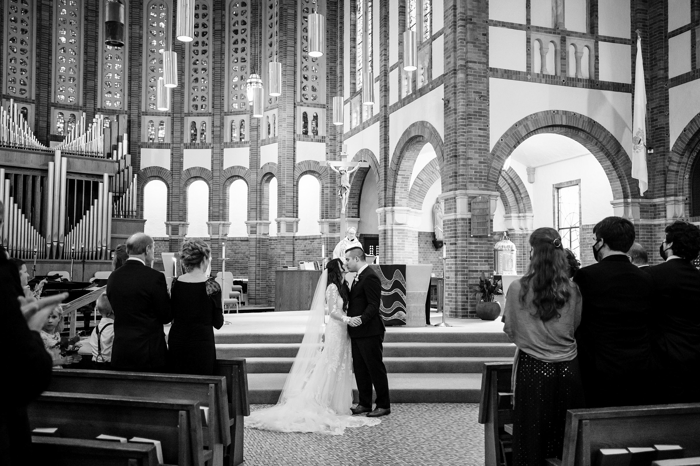 Faraway black and white shot of the bride and groom kissing during their wedding ceremony while guests and loved ones watch for their Ann Arbor intimate wedding by Detroit Wedding Photographer Michele Maloney