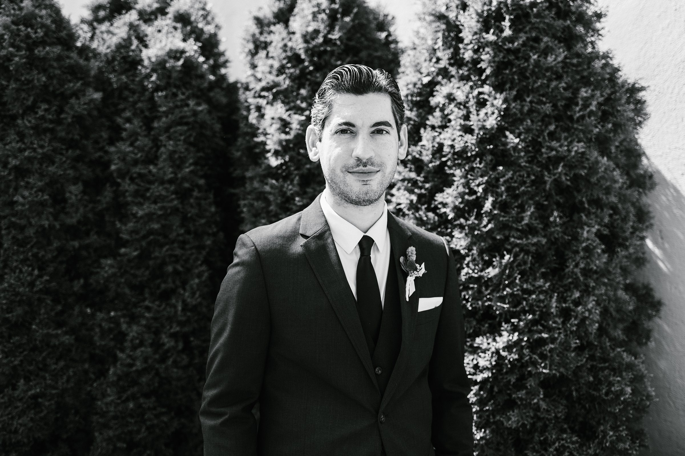Black and white portrait of the groom lightly smiling for the camera outside by Detroit Wedding Photographer Michele Maloney