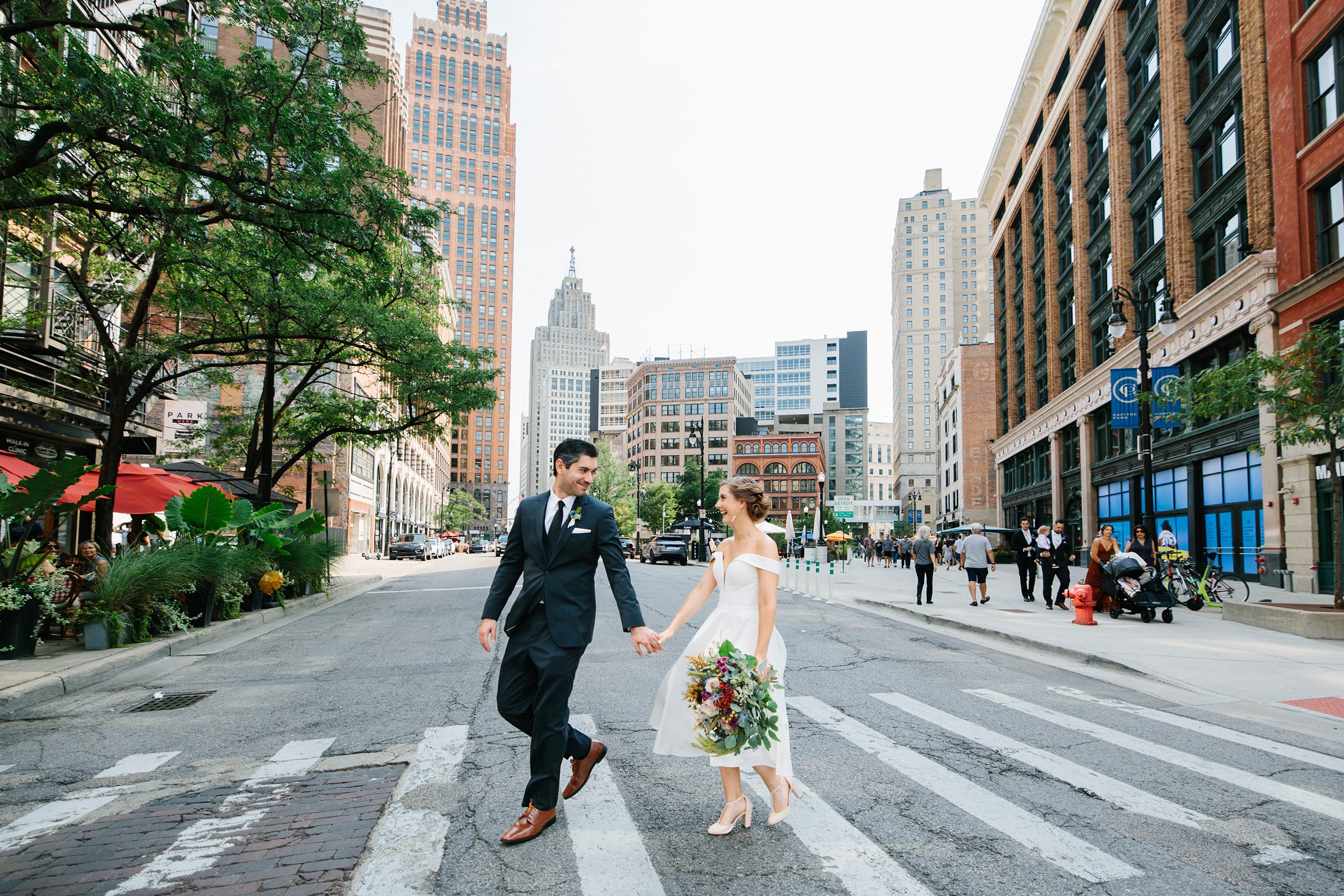 Bride and groom hold hands and stroll across a walkway in Detroit by Detroit Wedding Photographer Michele Maloney