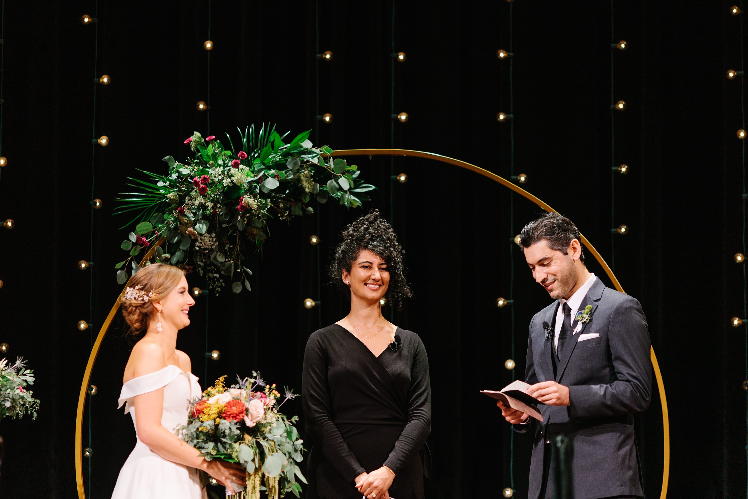 Bride and officiant smile as the groom is reading his vows to his bride during the Gem Theater Wedding by Detroit Wedding Photographer Michele Maloney 