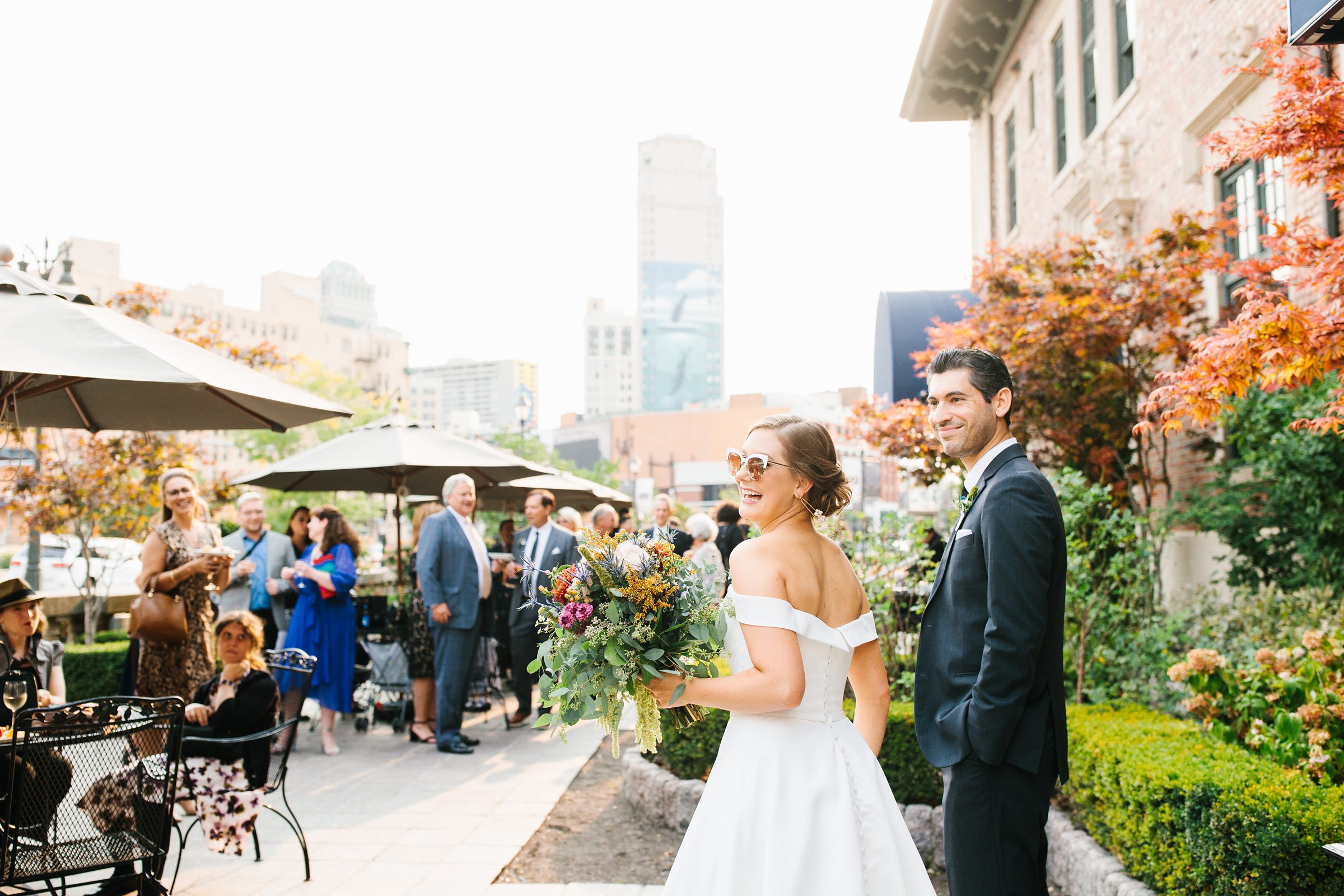 Newly married couple approach guests after their Gem Theater wedding, bride is wearing sunglasses and laughing by Detroit Wedding Photographer Michele Maloney