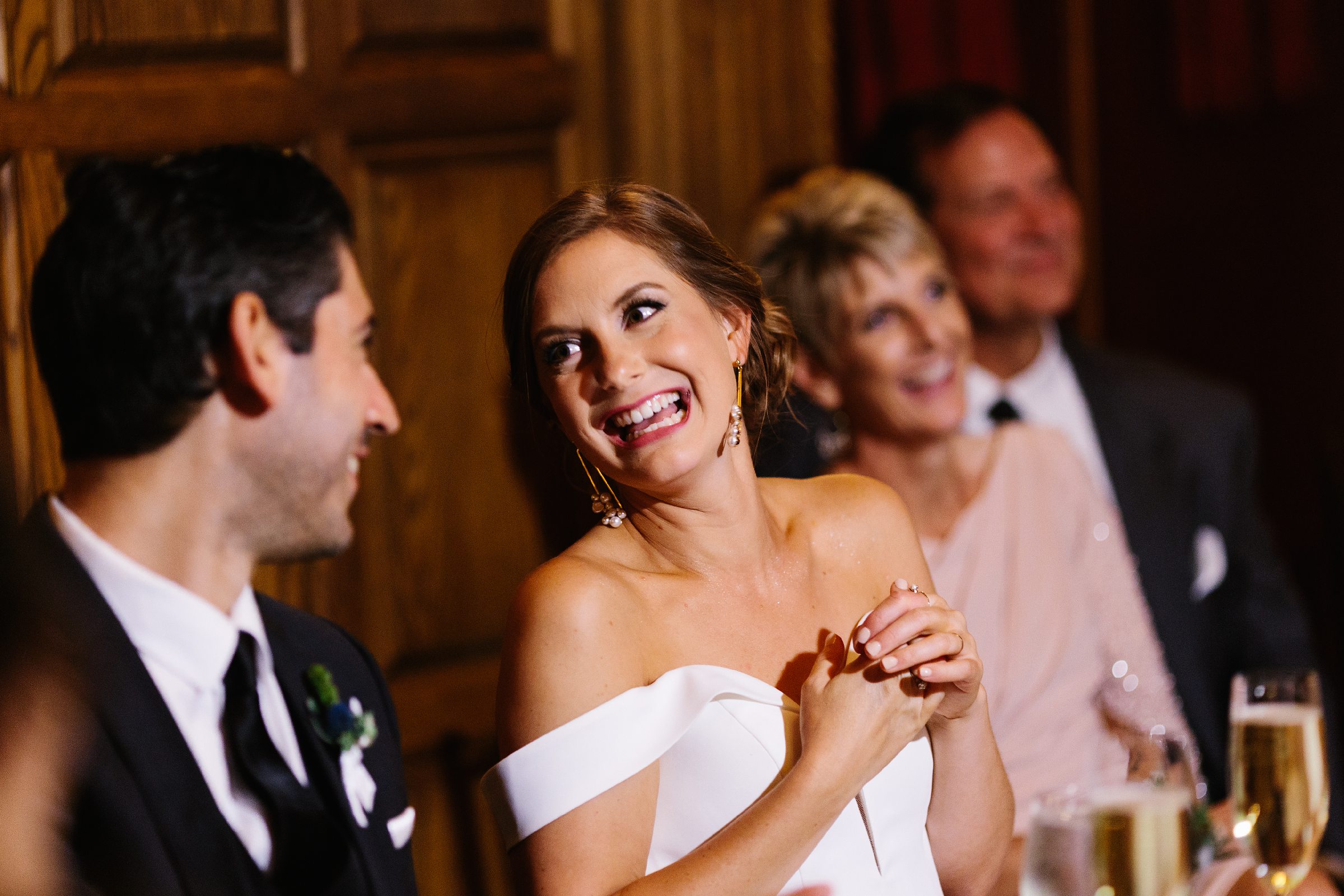 Bride laughs and looks at groom during wedding toasts by Detroit Wedding Photographer Michele Maloney