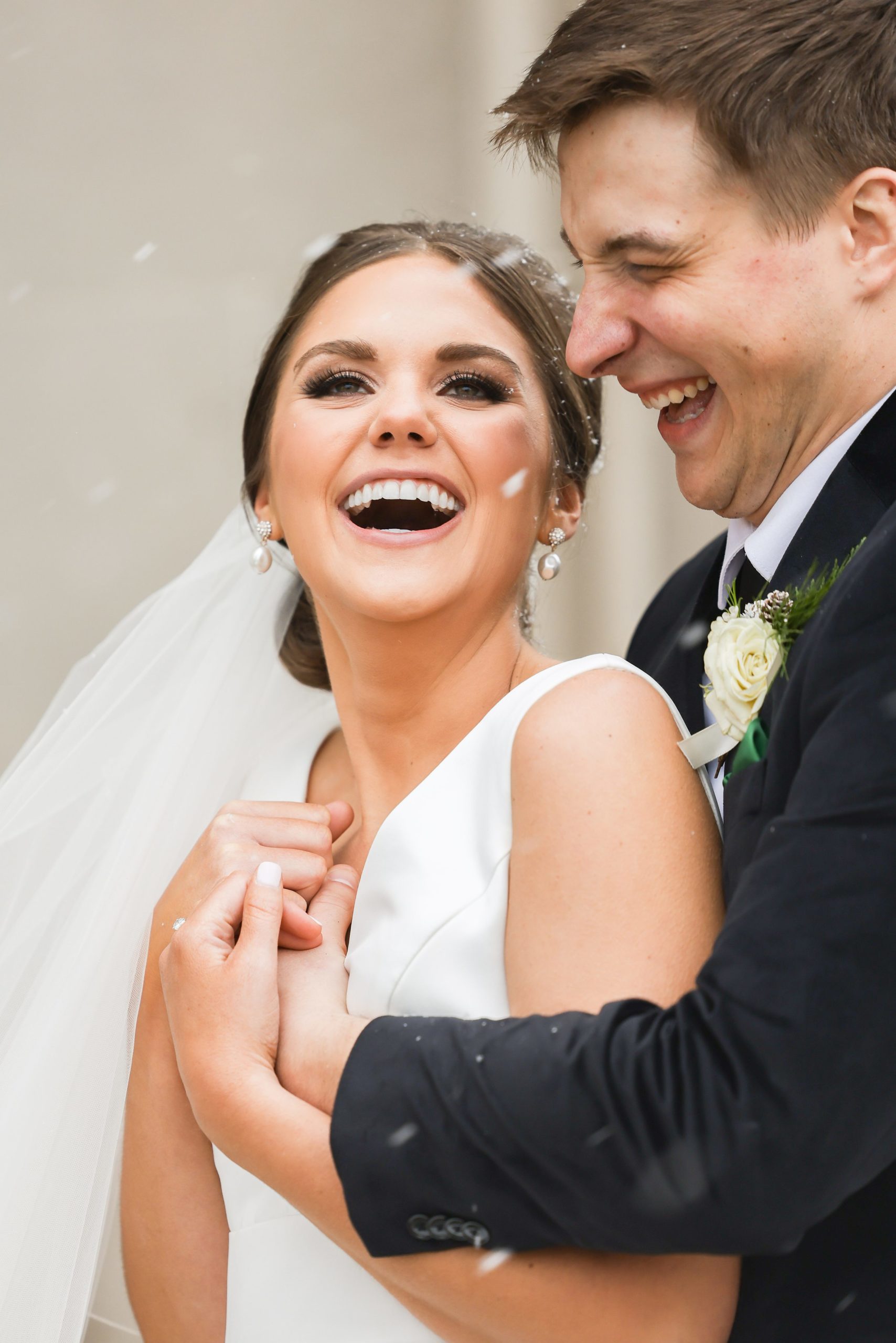 Bride and groom laugh as groom hugs bride from behind as it snows by Detroit Wedding Photographer Michele Maloney
