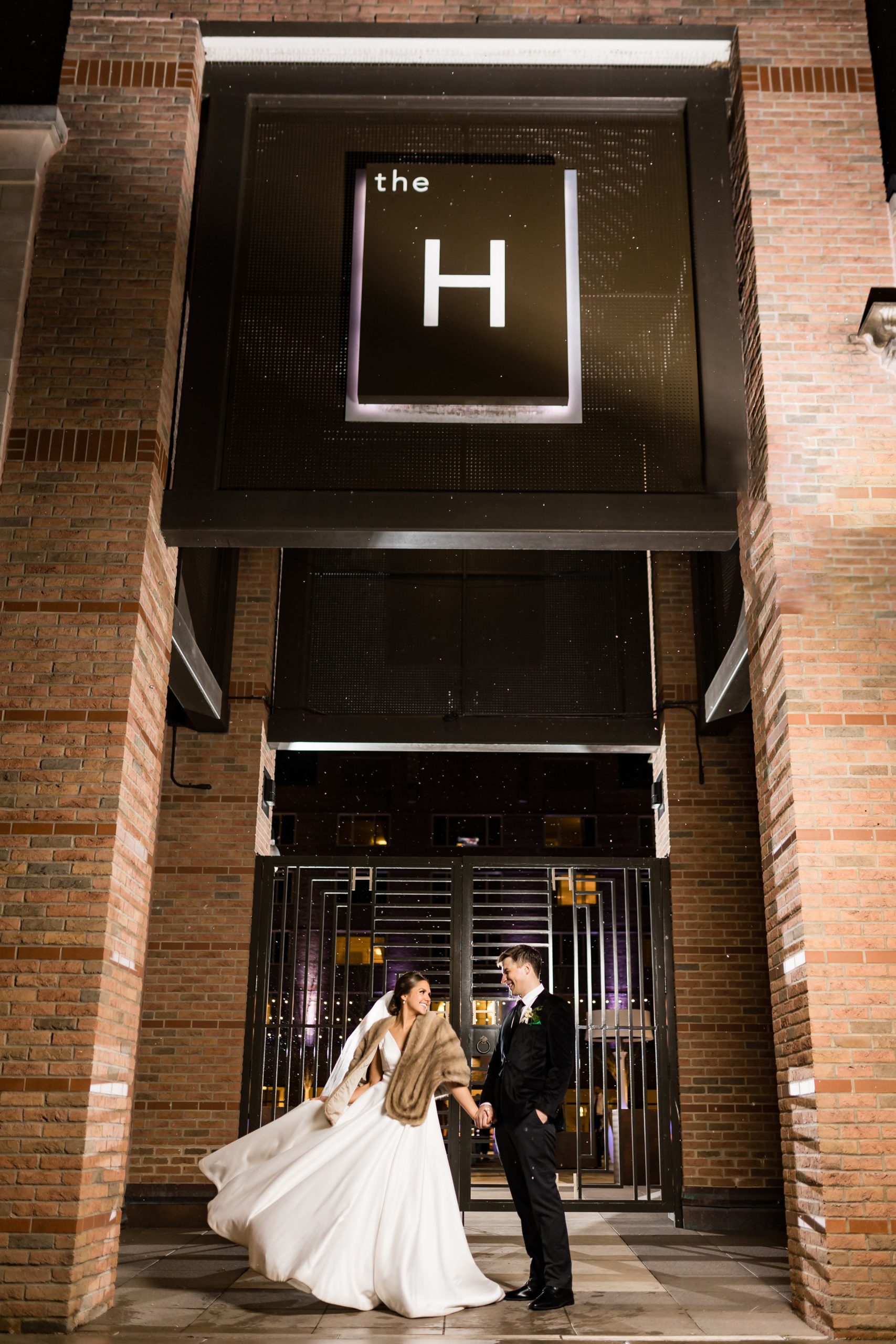 Bride and groom hold hands and smile outside of the H Hotel by Detroit Wedding Photographer Michele Maloney