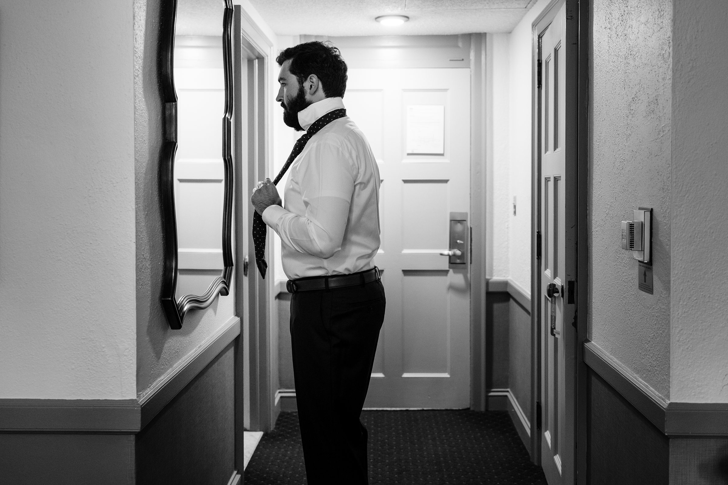Black and white photo of the groom looking in the mirror as he gets ready by Detroit Wedding Photographer Michele Maloney