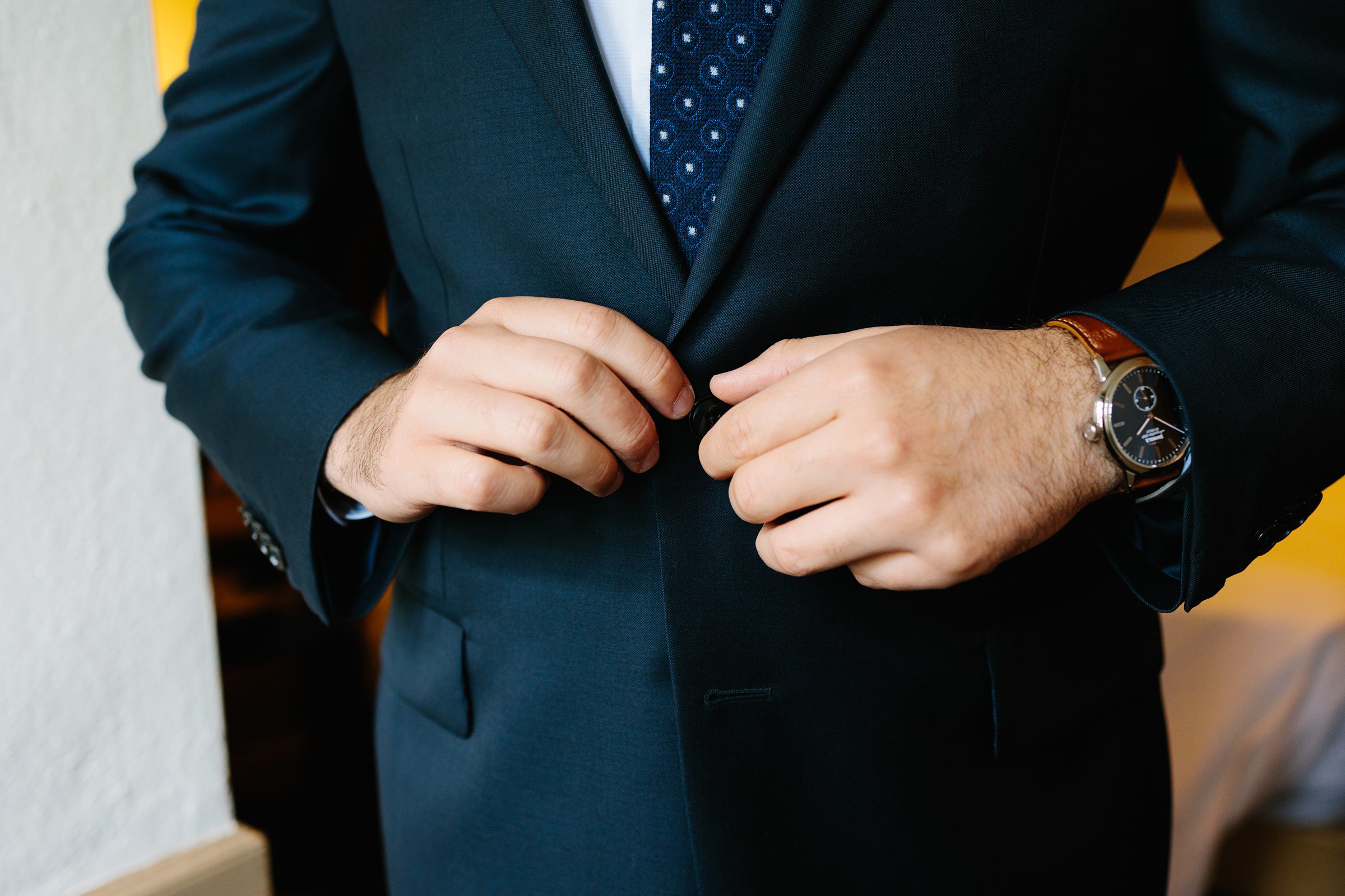 Close up of groom's hands buttoning up his suit as he gets ready for the ceremony by Detroit Wedding Photographer Michele Maloney