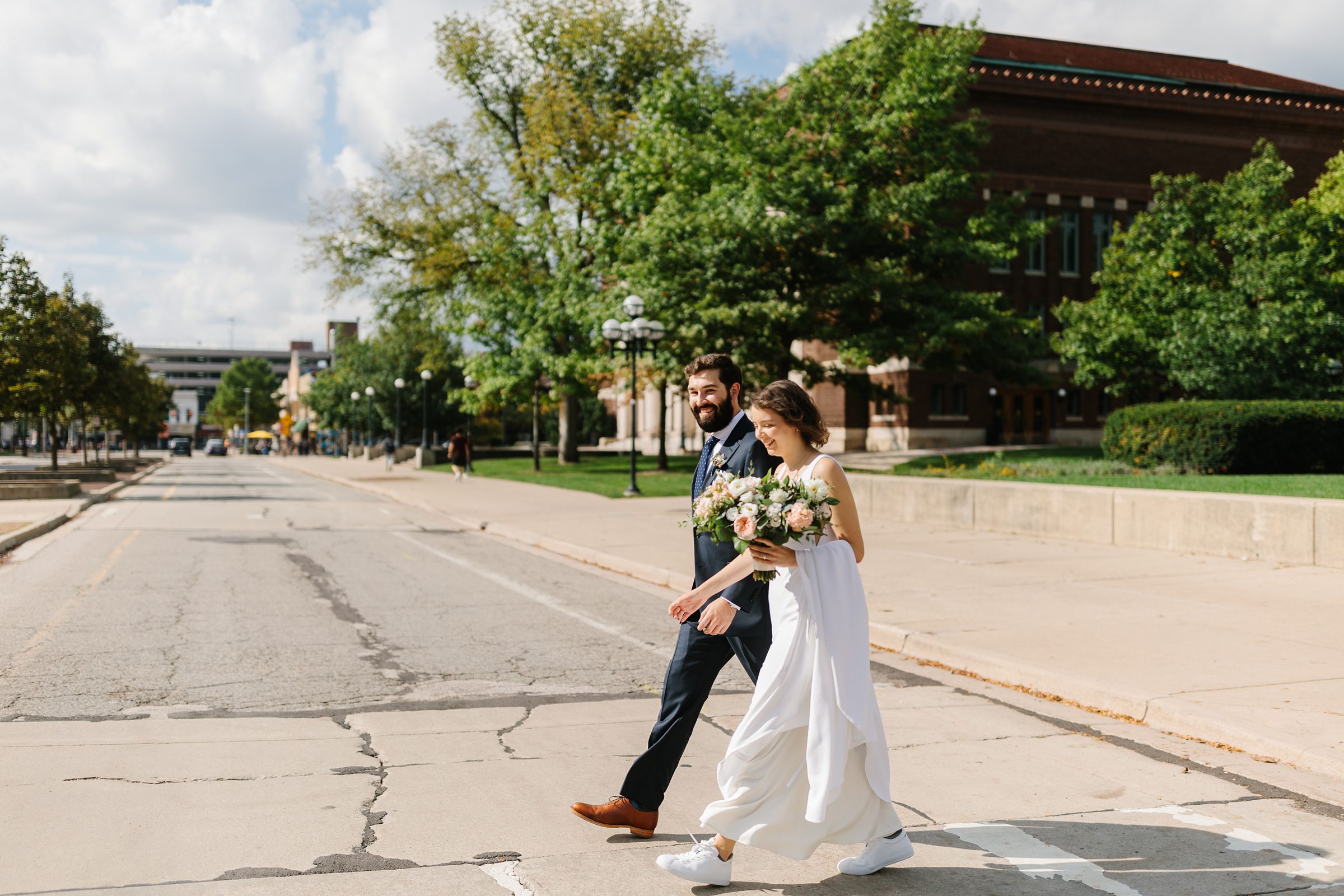 Bride and groom link arms and cross the street during their first look session by Detroit Wedding Photographer Michele Maloney