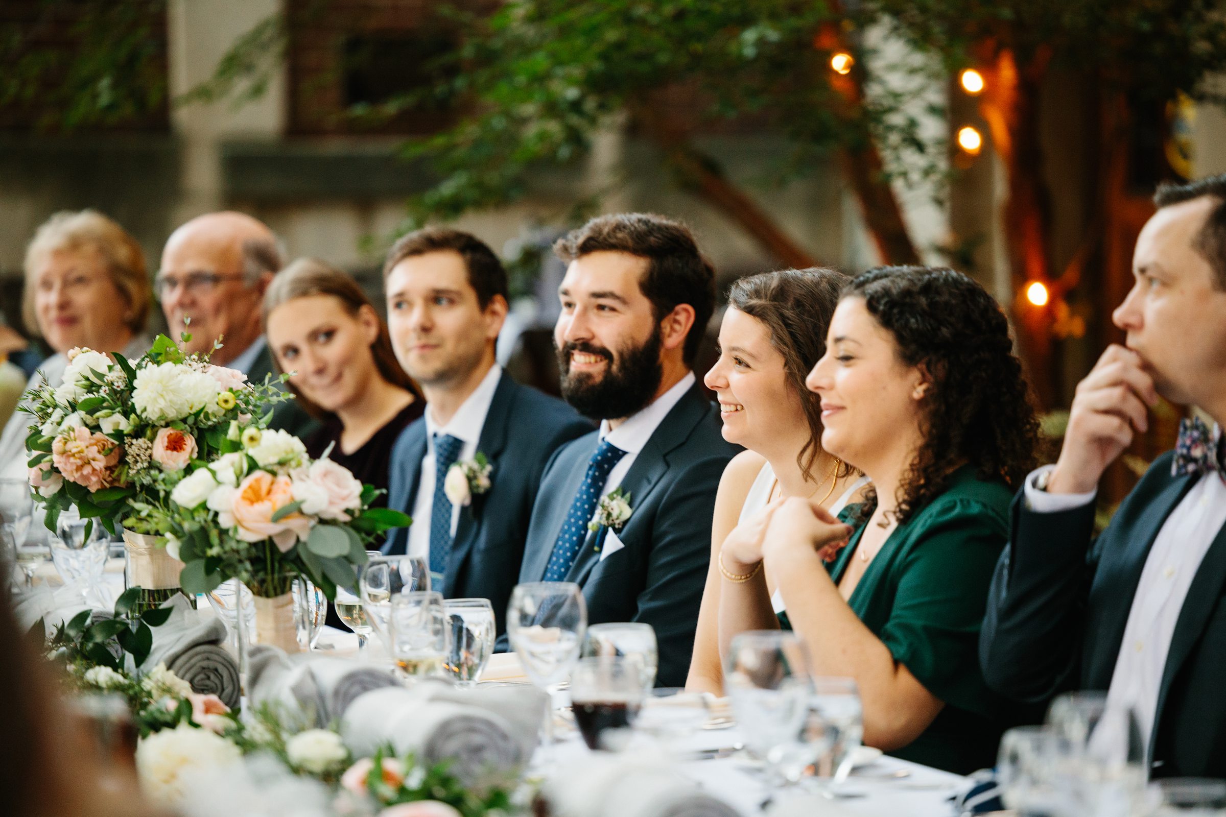 Bride and groom sit with their wedding party at the reception for The Inn at the Michigan League Wedding by Detroit Wedding Photographer Michele Maloney