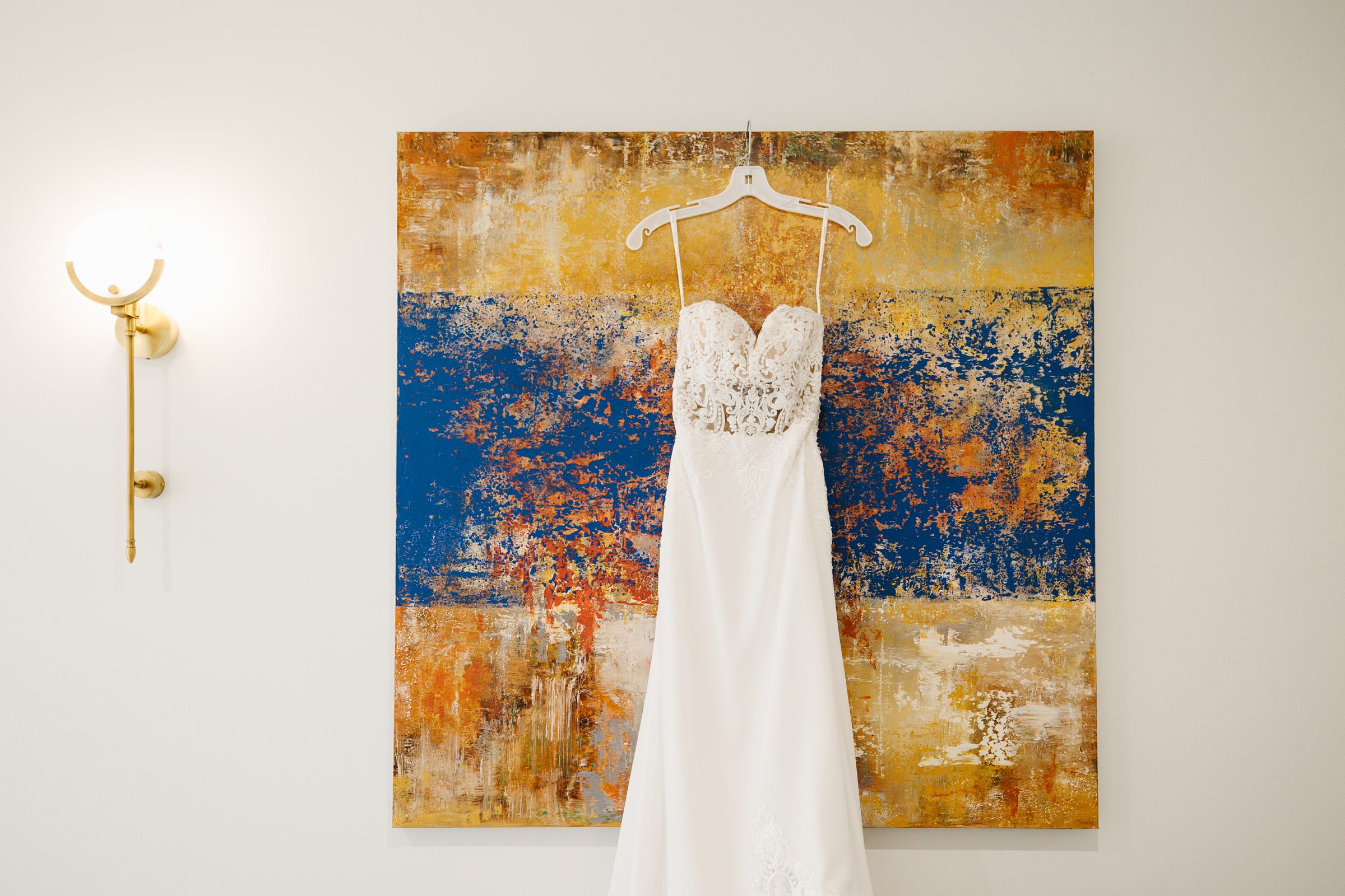 Wedding dress hangs on abstract painting by Detroit Wedding Photographer Michele Maloney