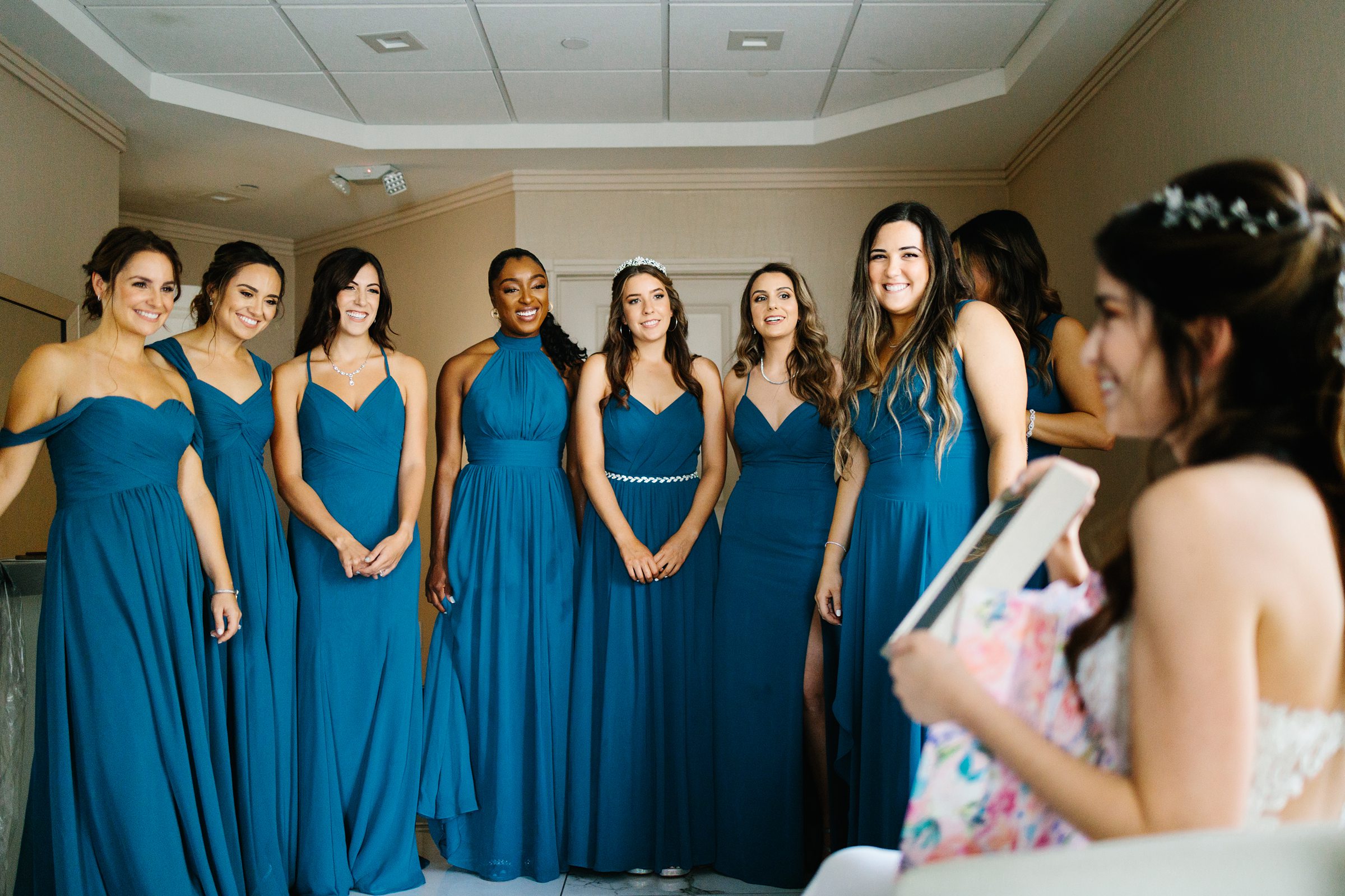 Bridesmaids smile at bride opening gift while they get ready by Detroit Wedding Photographer Michele Maloney