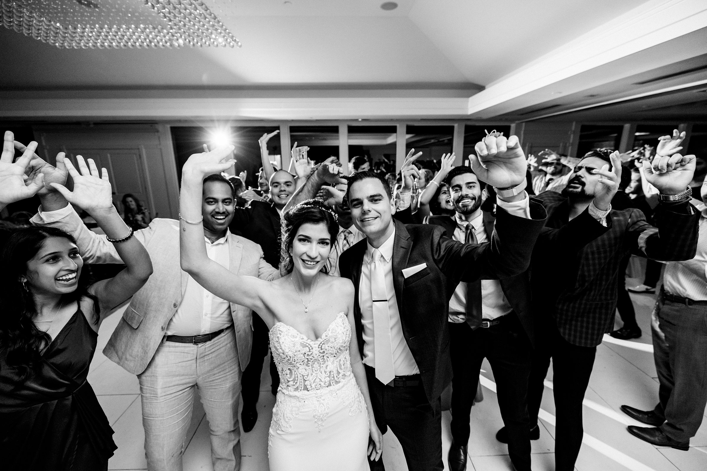 Black and white photo of guests, bride, and groom with their hands up dancing and all looking at the camera by Detroit Wedding Photographer Michele Maloney