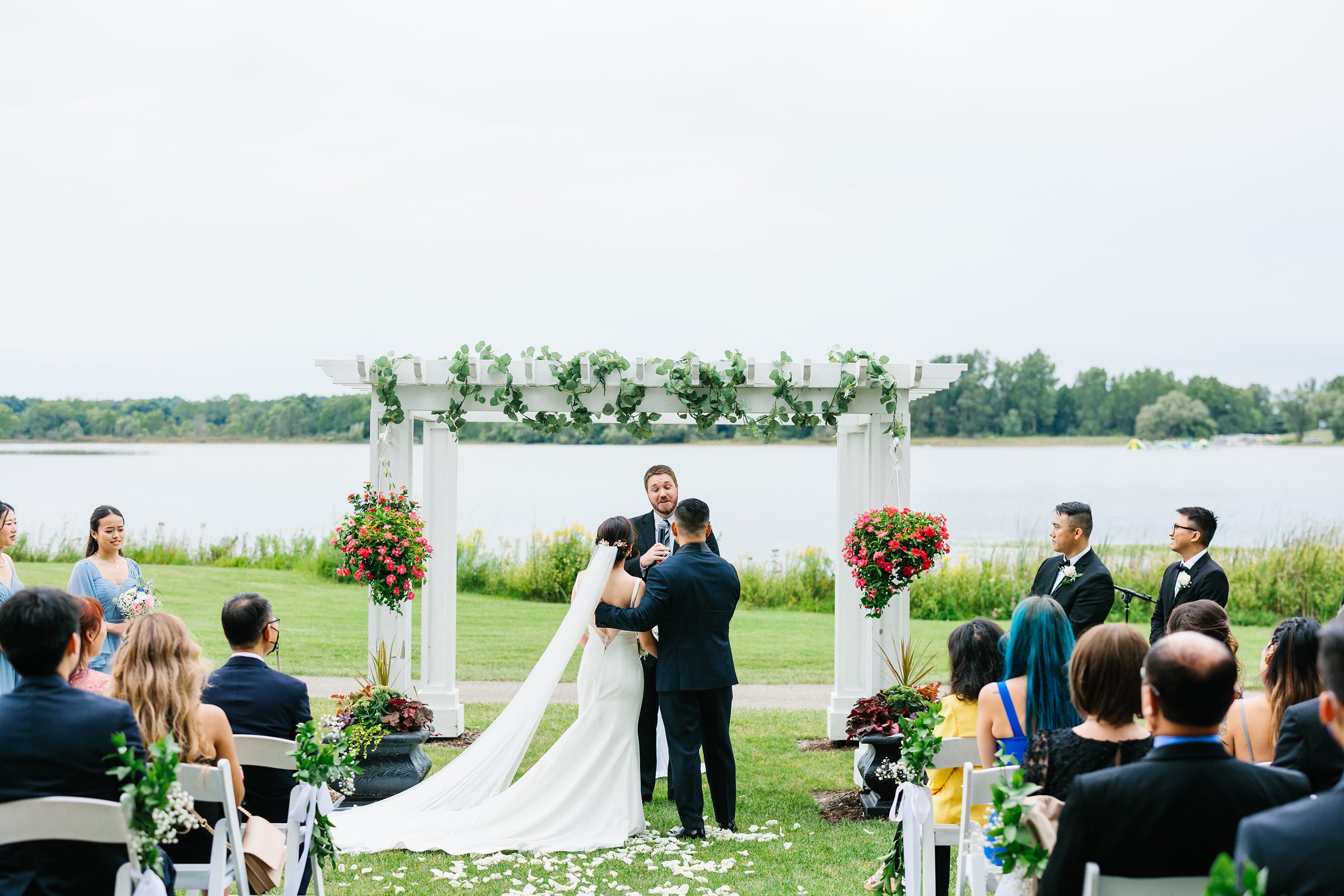 Bride and groom face the pastor during their outdoor ceremony at Waldenwoods while guests and bridal party watch by Detroit Wedding Photographer Michele Maloney 