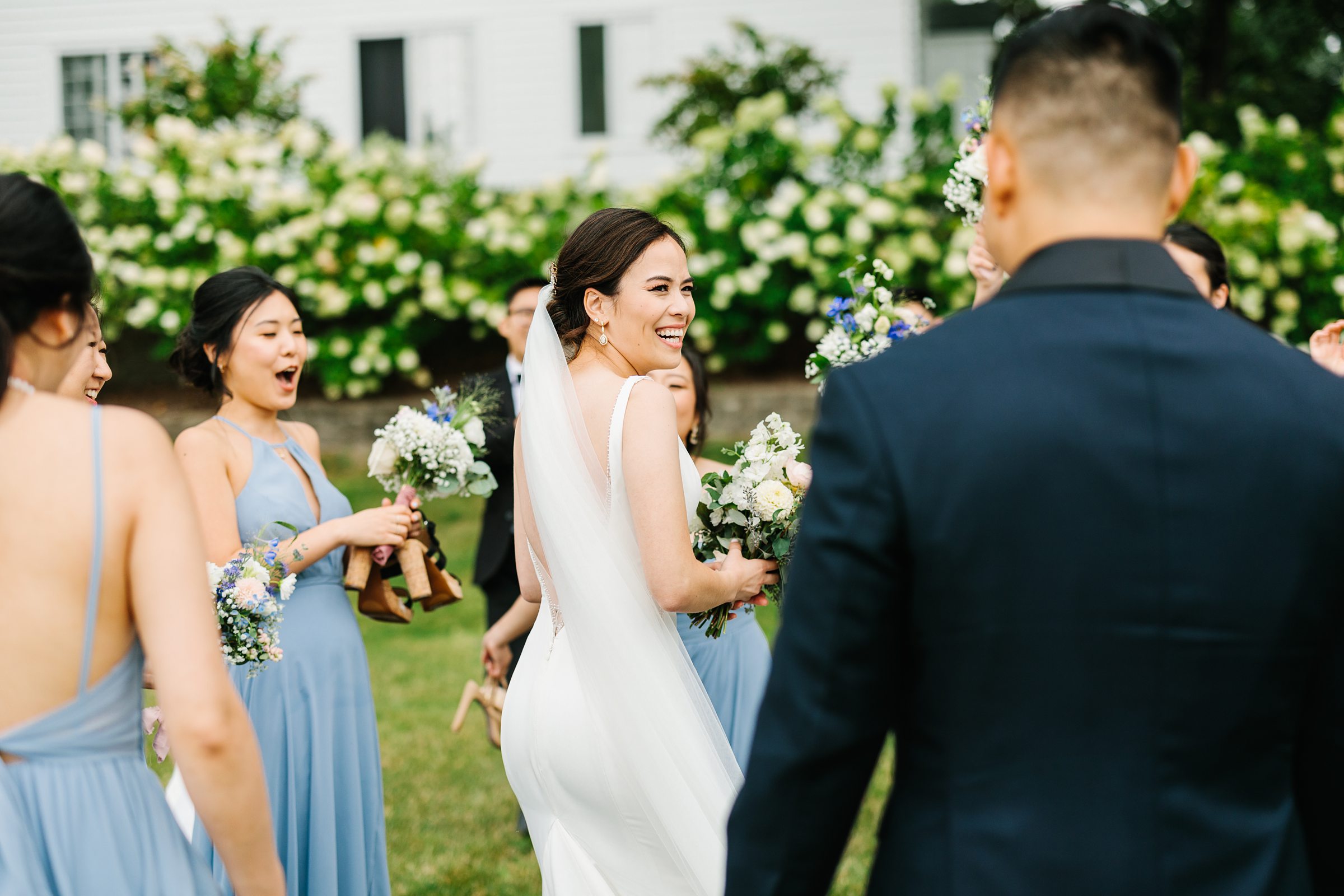 Bride looks over and smiles, surrounded by loved ones at her Walenwoods summer wedding by Detroit Wedding Photographer Michele Maloney