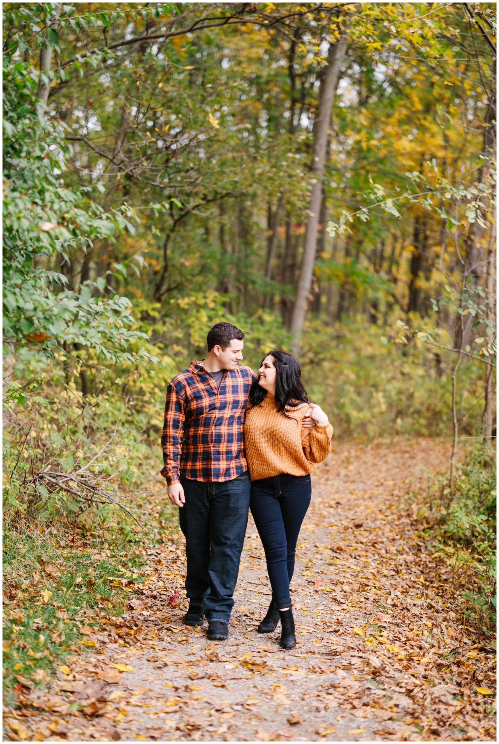 Engaged couple strolls through Kensington Metropark while staring at each other by Detroit Wedding Photographer Michele Maloney