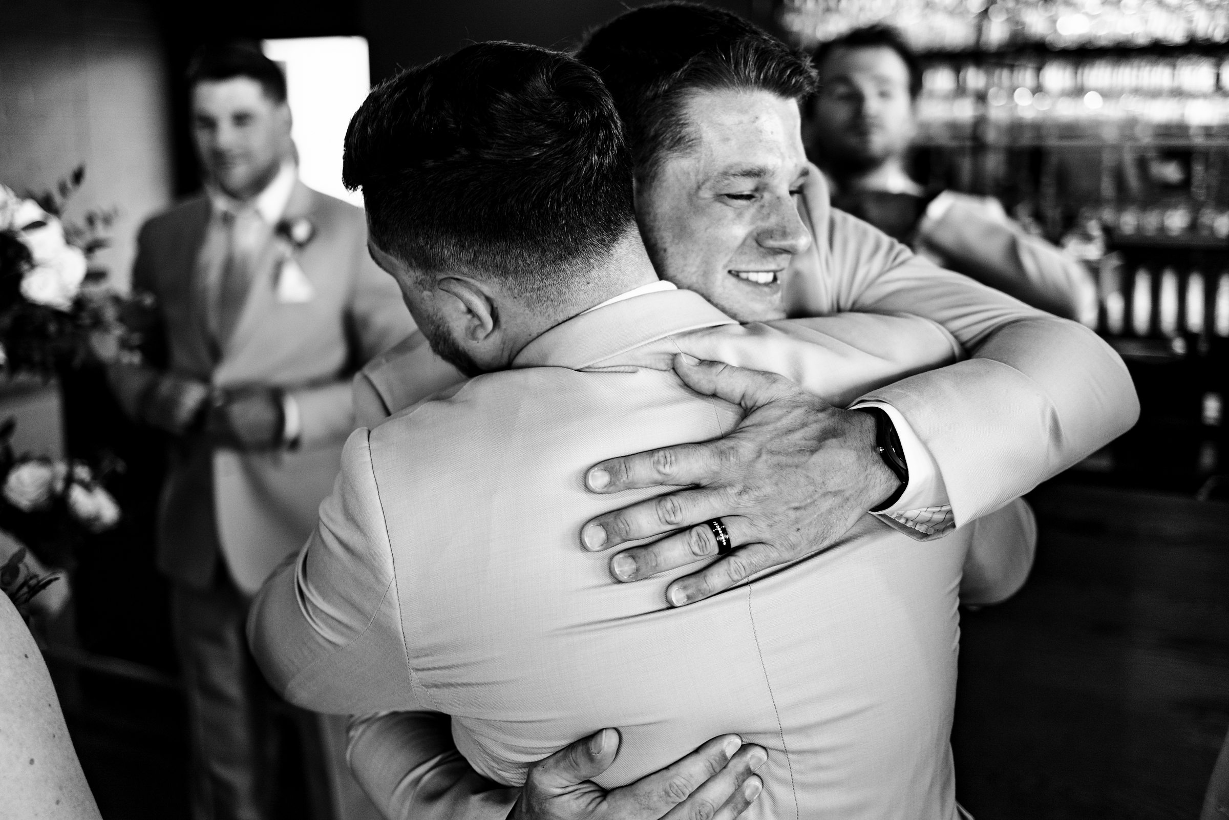 Candid moment of groom hugging groomsmans at Port 393 in Holland Michigan by Michele Maloney Photography