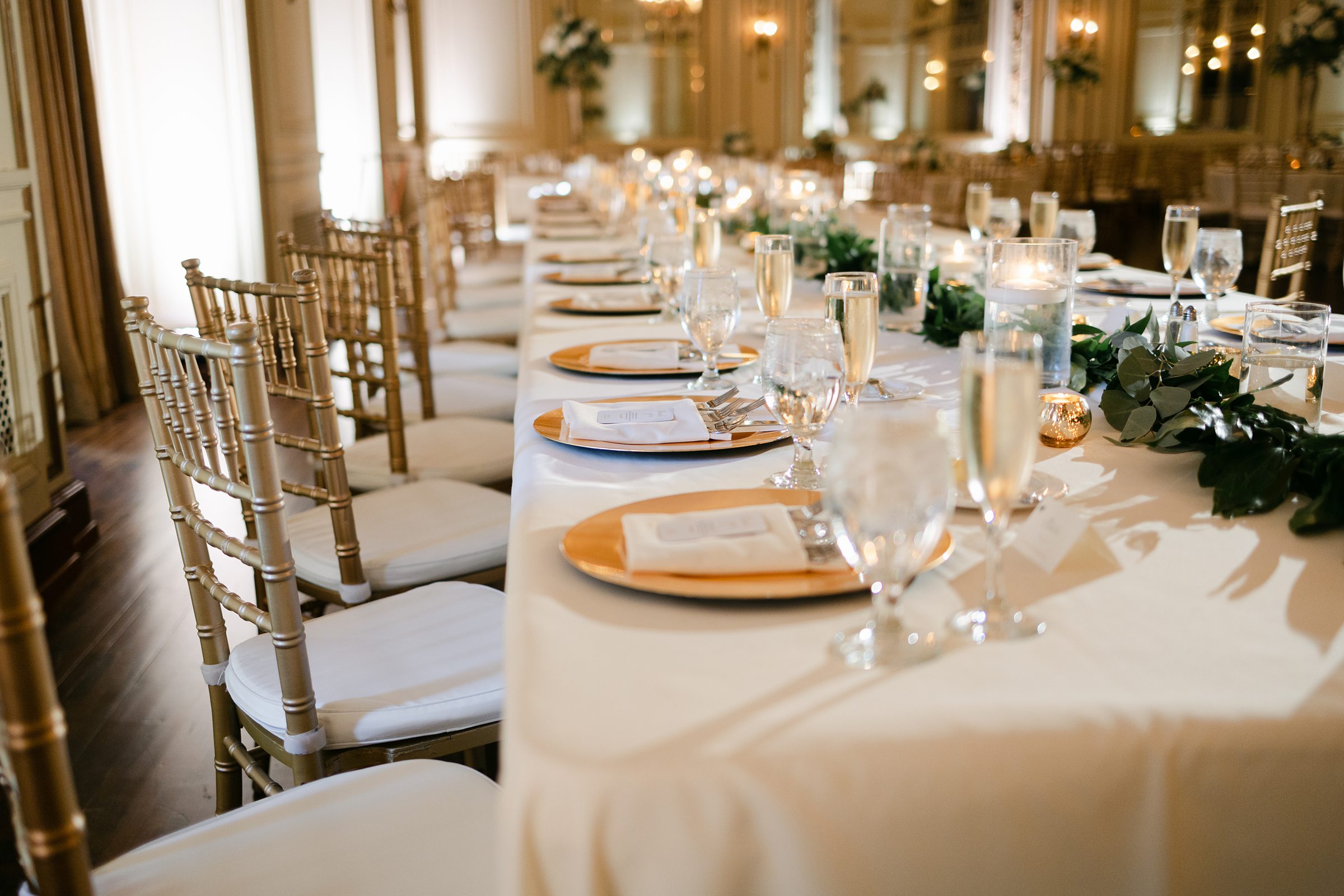 Head Table with white and gold table settings at indoor wedding reception