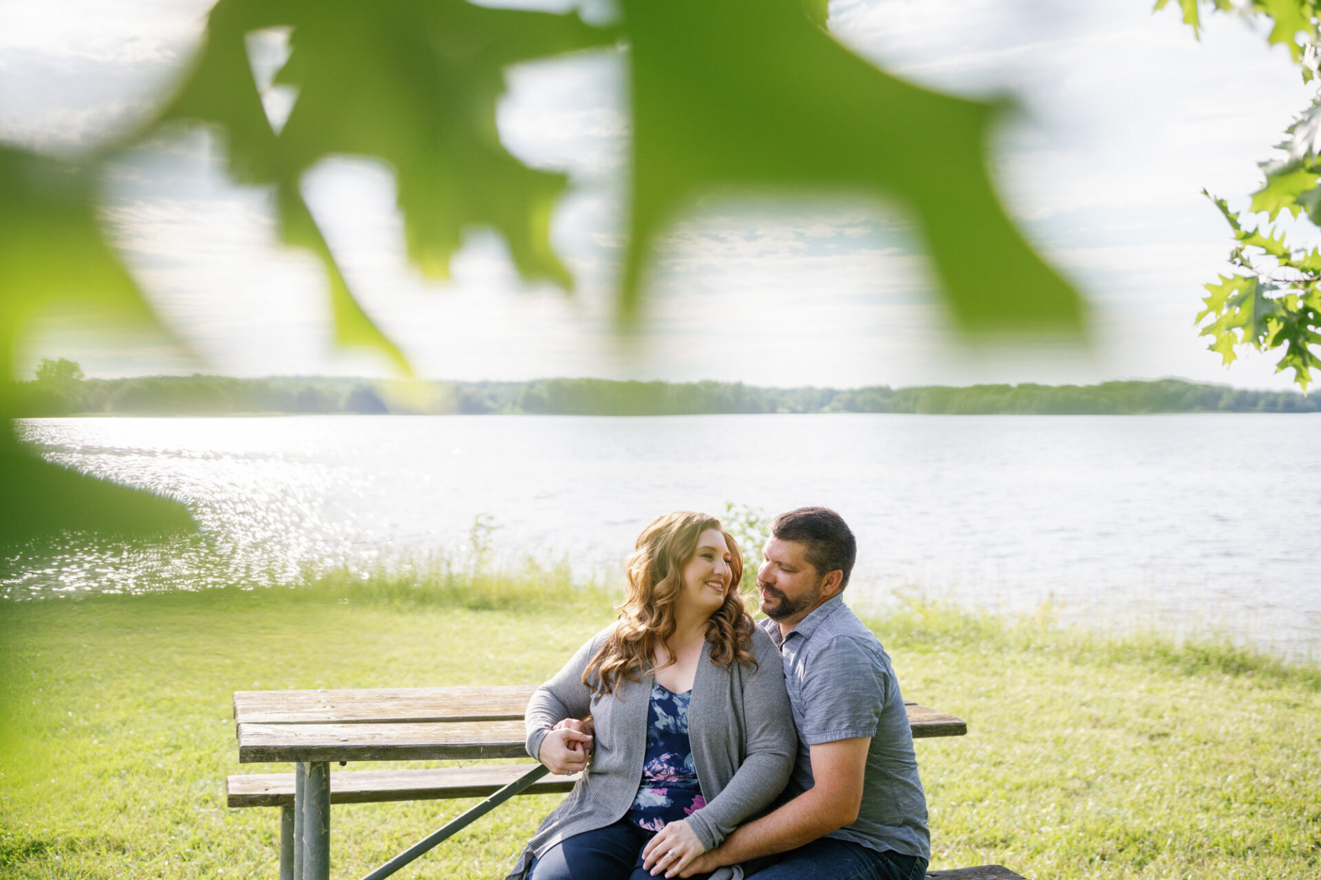 couple sitting near the lake at their summer engagement session at stoney creek metropark