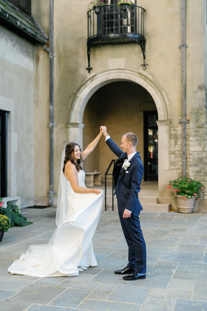 Bride and groom share a joyful moment dancing together in the stone courtyard at Kirk in the Hills