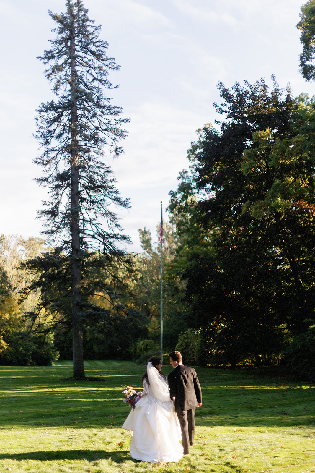 Bride and groom walking through The Village Club garden in fall light.